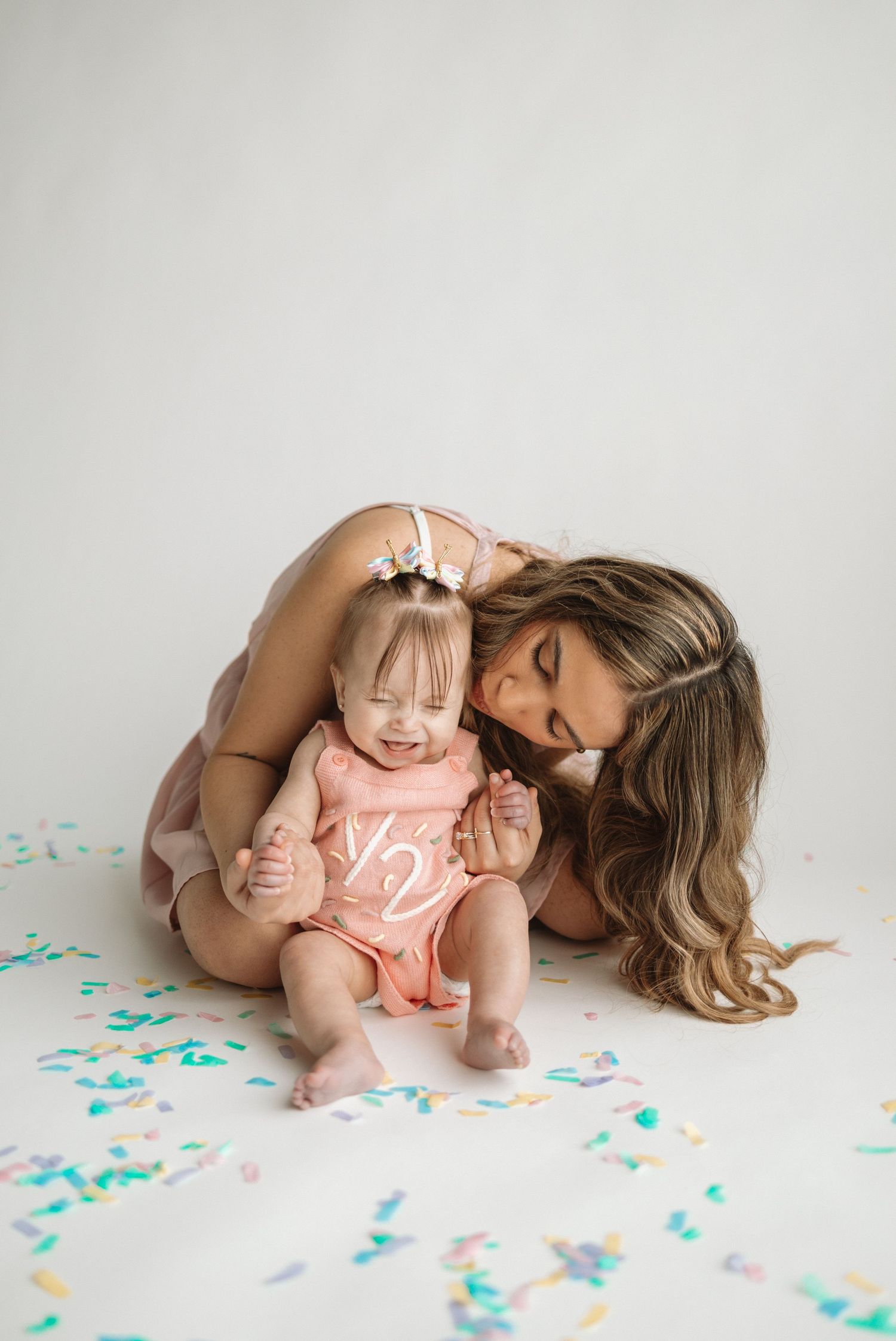 Sweet tender moment shared between parent and baby sitting on white floor with scattered colorful confetti.