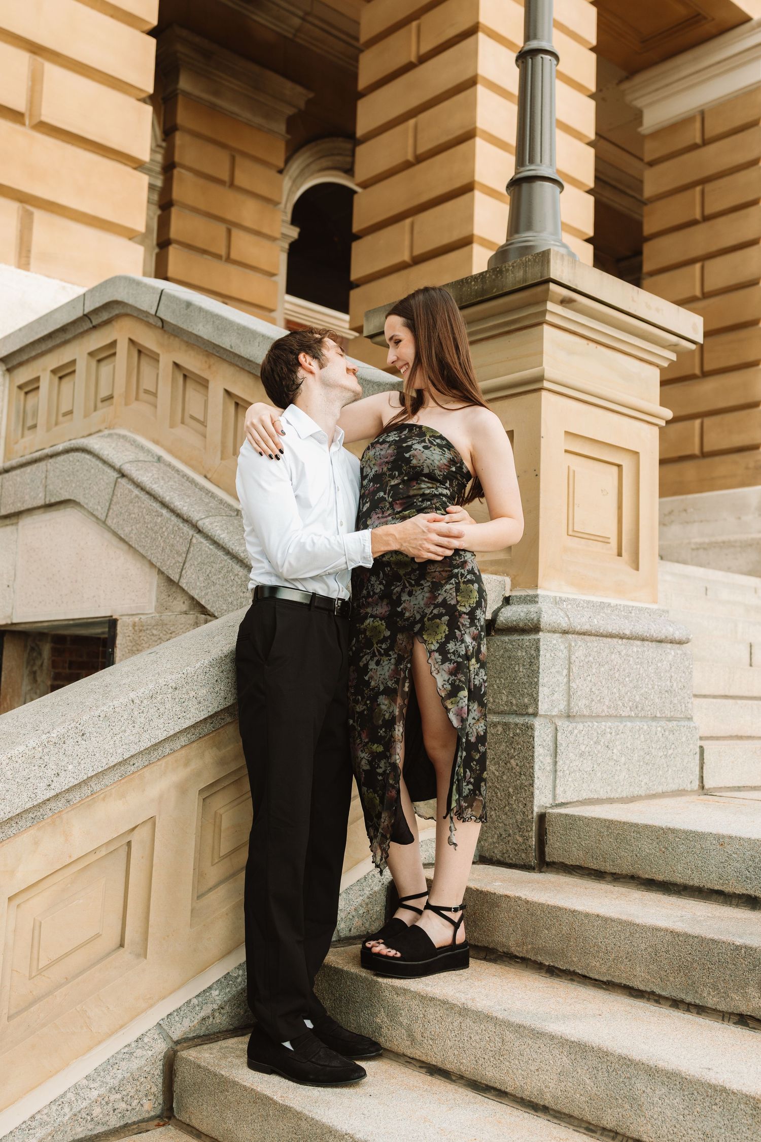 A couple shares a romantic moment on elegant stone steps of a historic building with cream colored walls.