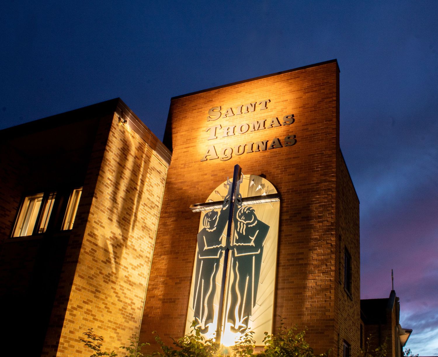 Illuminated brick facade of Notre Dame du Sablon church in Brussels glows warmly against the dark evening sky.