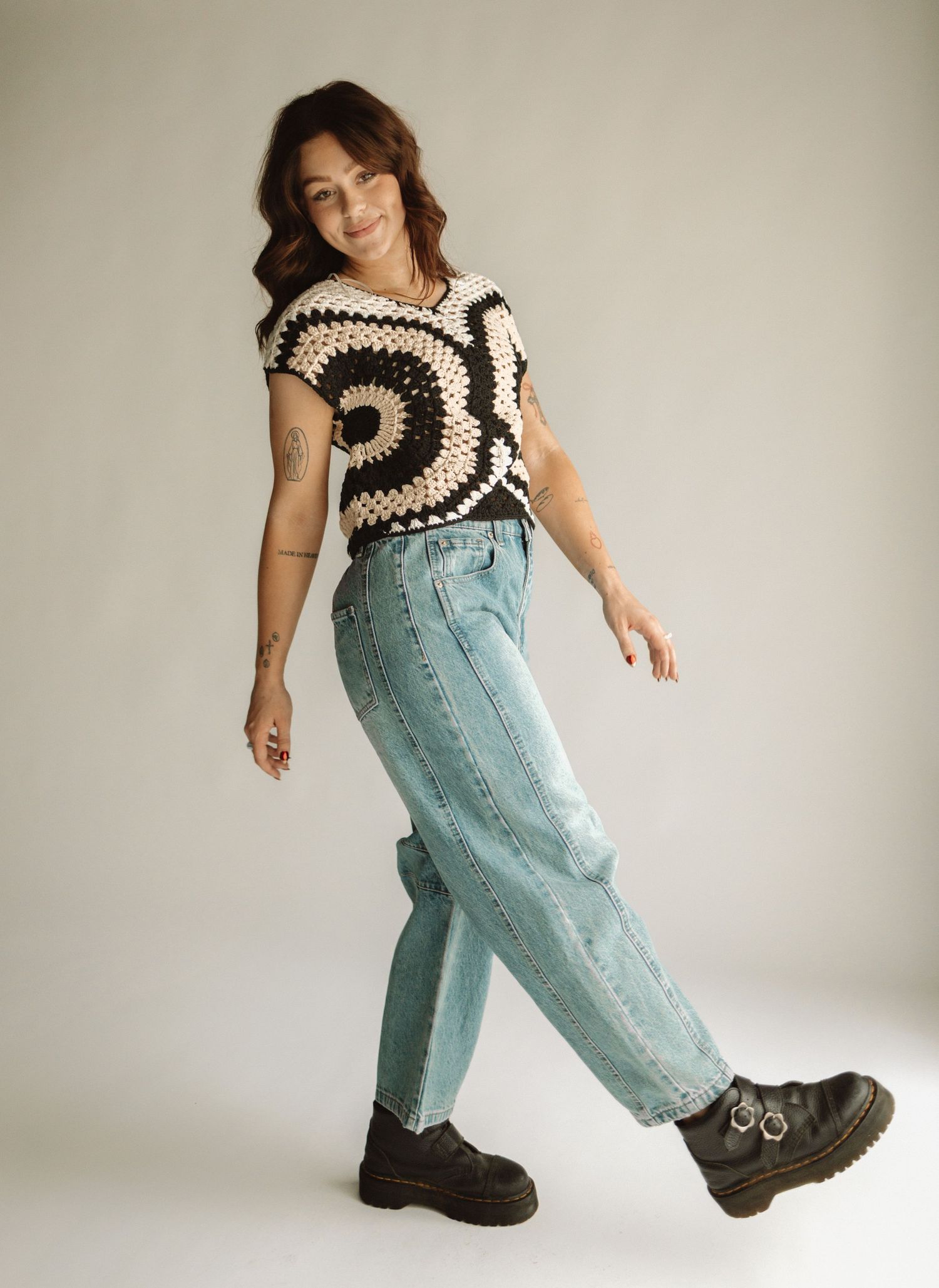 A person wearing a brown and cream striped top and light blue denim jeans poses playfully against a white background.