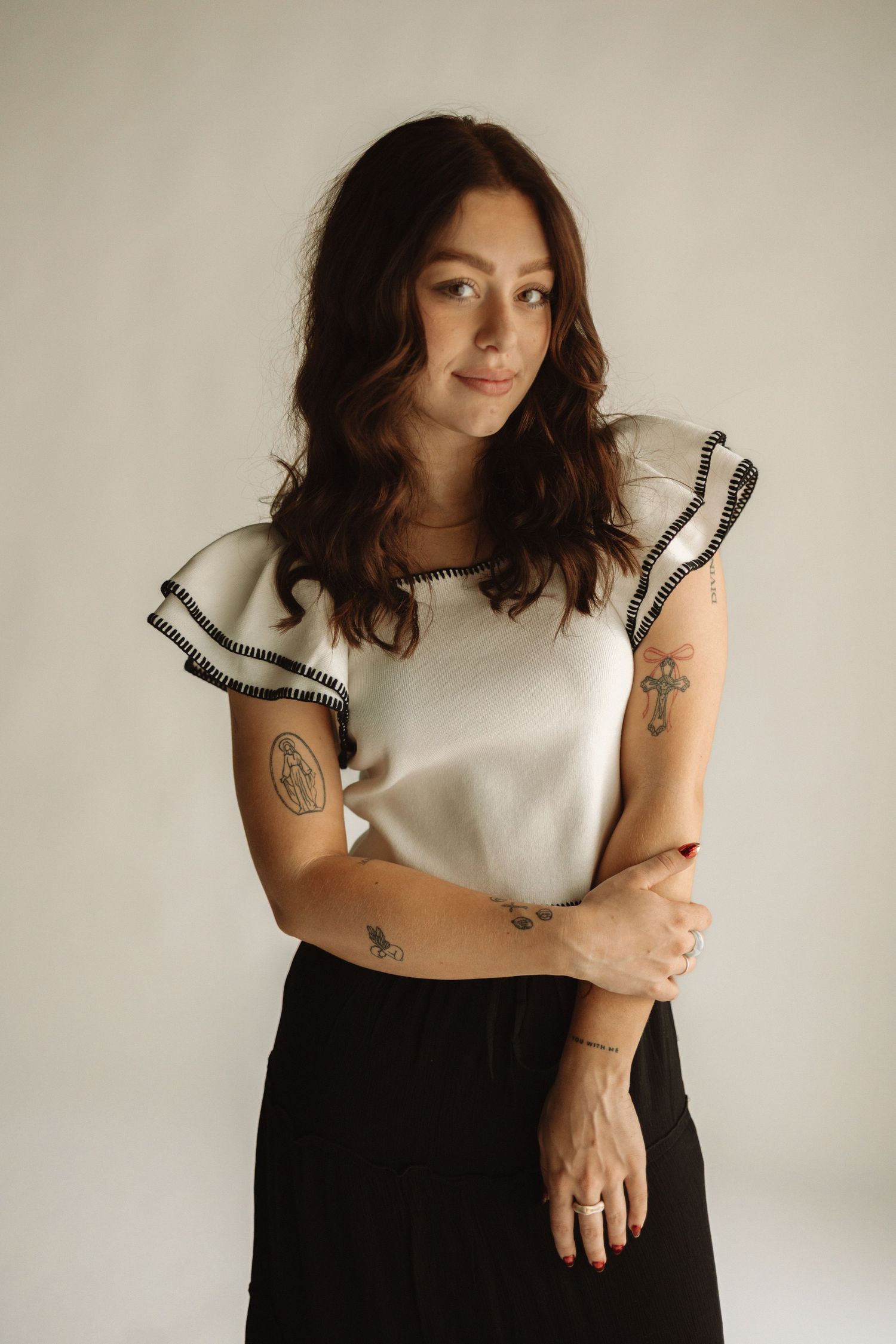 Person in white top and black bottoms sitting against neutral background showing tattoos and arm poses in artistic series.