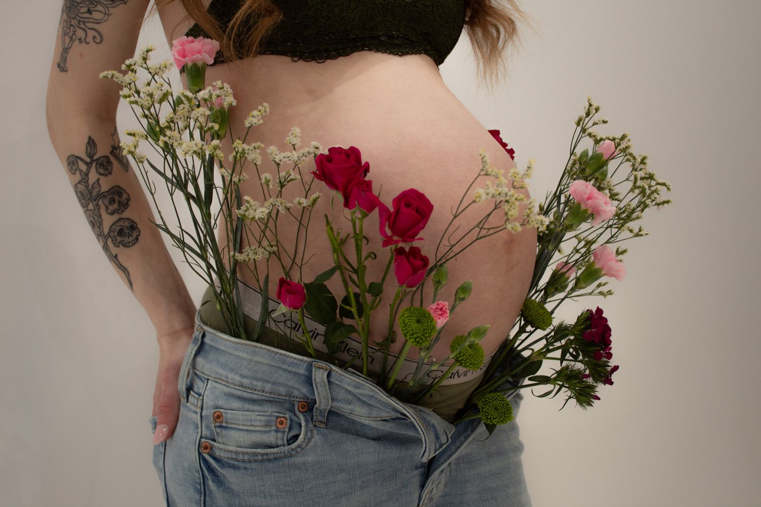 Fresh flowers including red roses and white baby's breath tucked into the back pocket of light wash denim jeans.