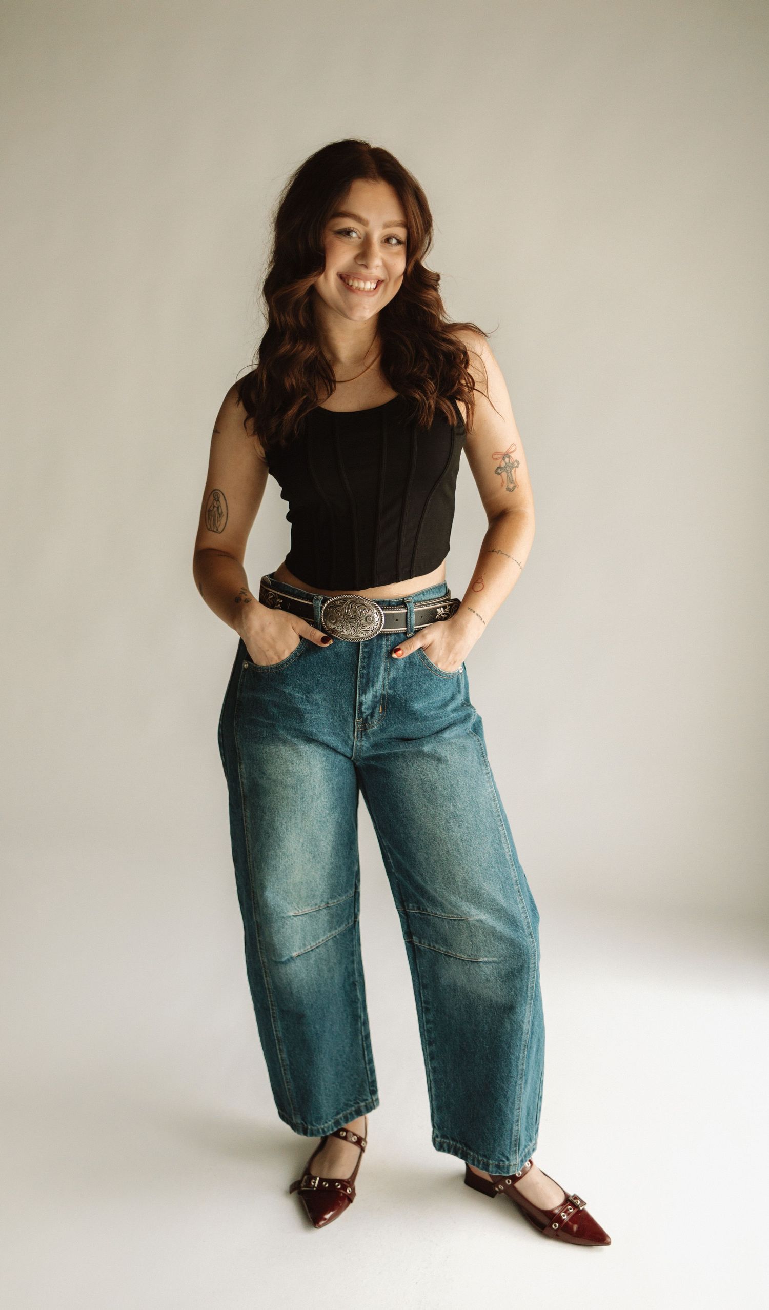 Casual fashion look featuring loose-fit denim jeans, black tank top, leather belt and burgundy flats against white backdrop.
