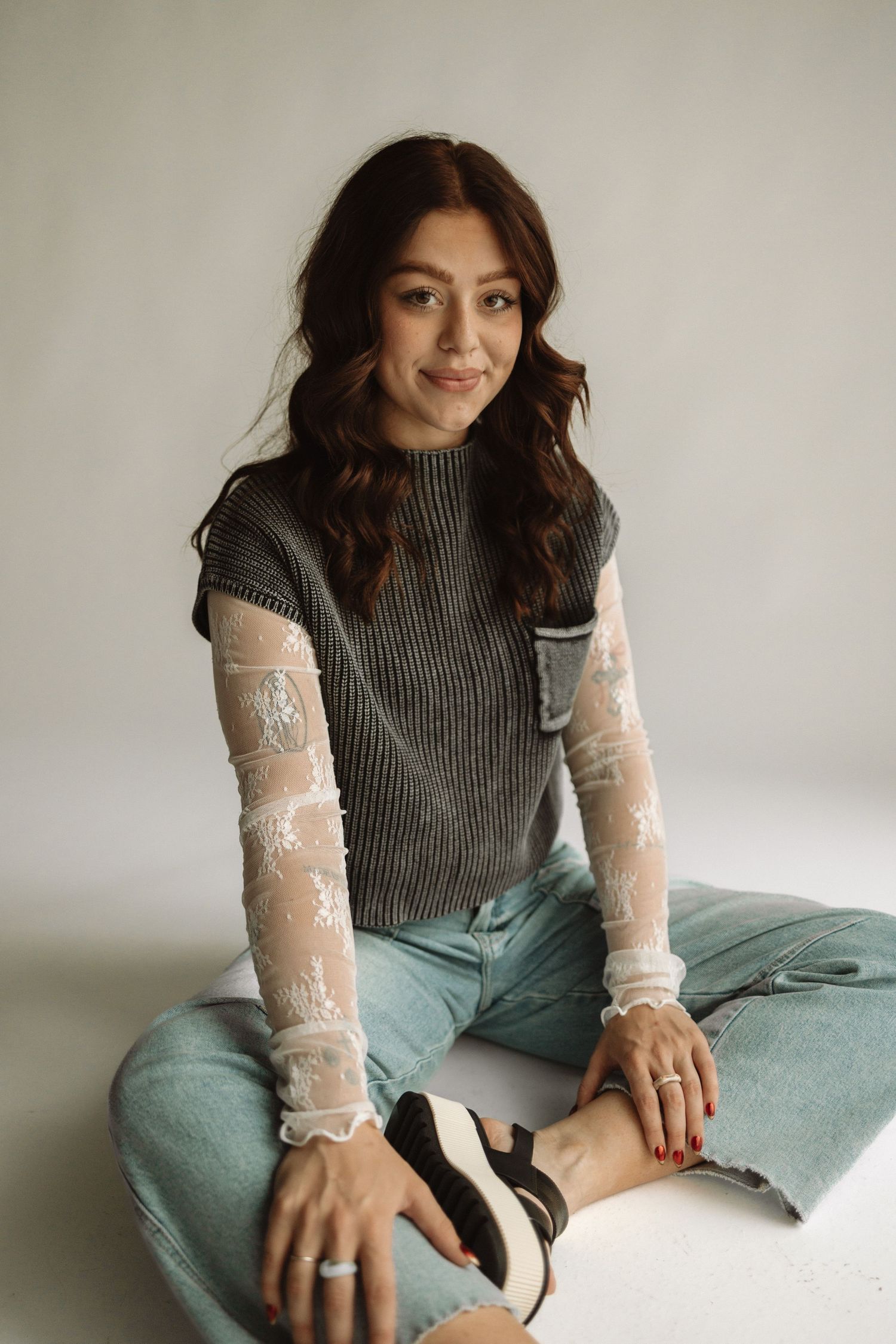 Fashion portrait showing grey turtleneck vest paired with sheer lace sleeves and light denim in studio setting.