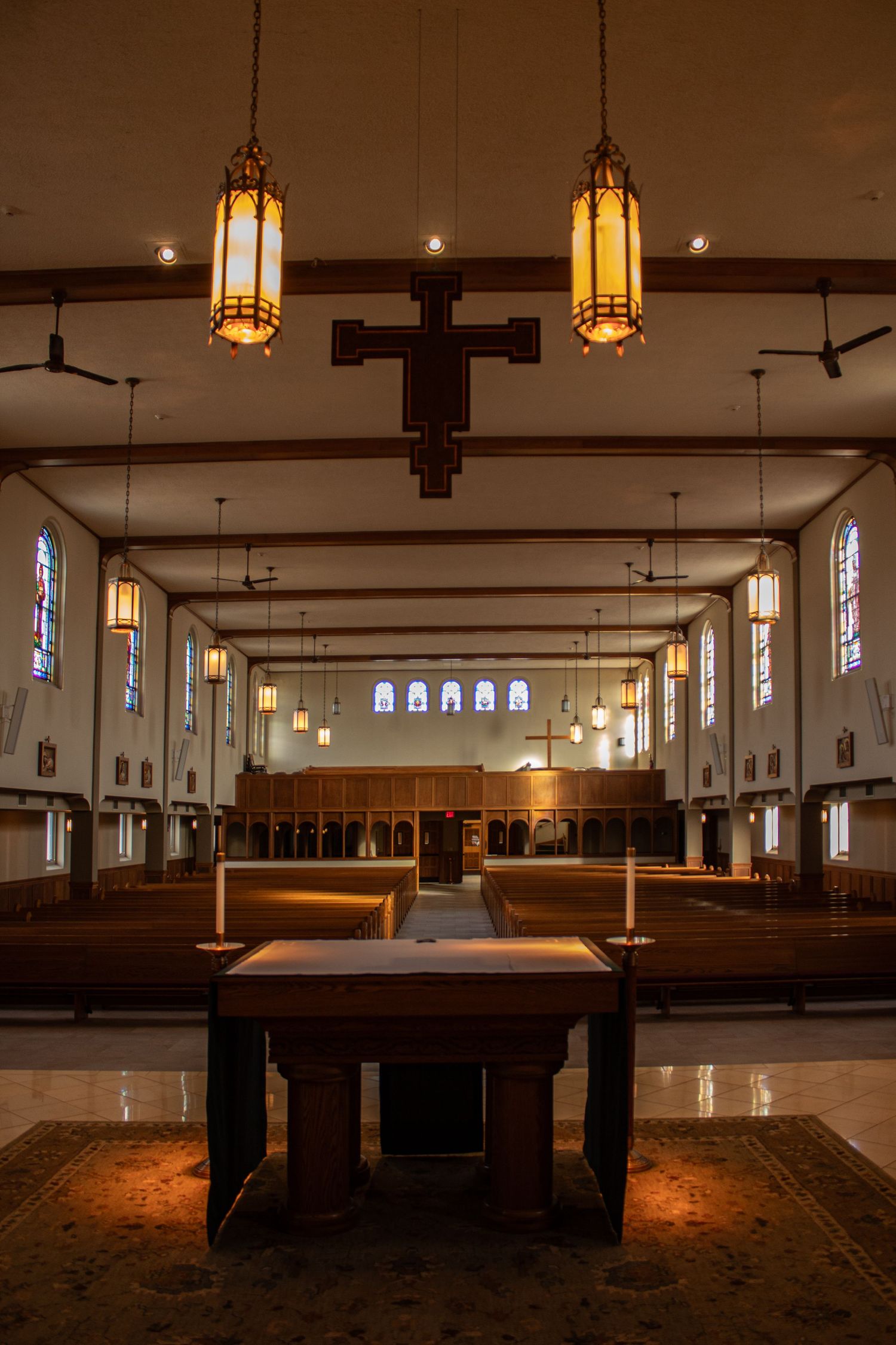 Interior panorama of a church sanctuary with wooden pews and hanging pendant lights illuminating the simple sacred space.