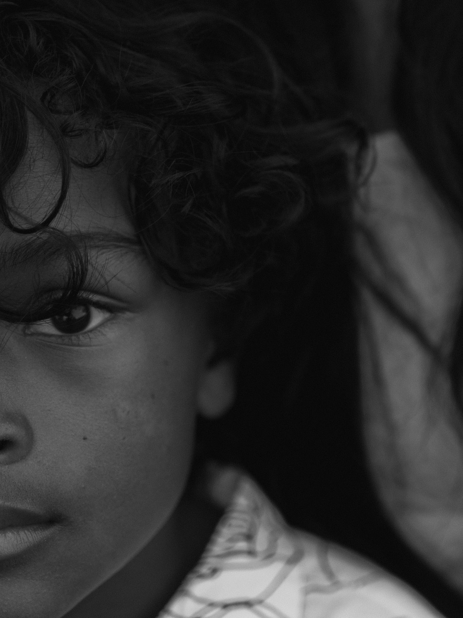 A black and white artistic portrait showing an extreme close-up view of an eye and curly hair.