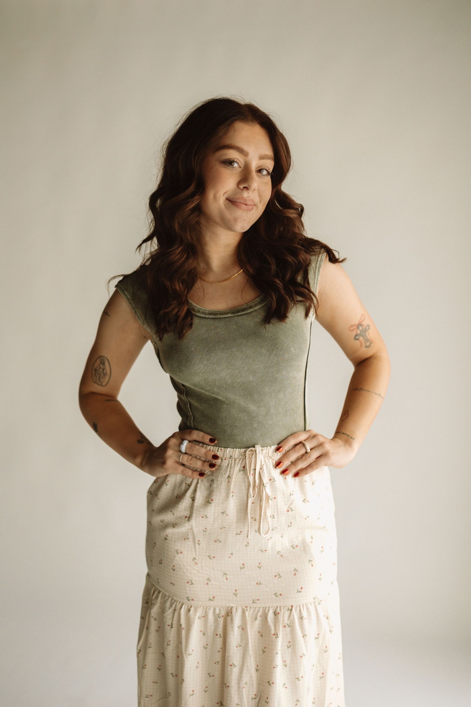 A person in a casual olive tank top and patterned cream maxi skirt poses against a neutral background.
