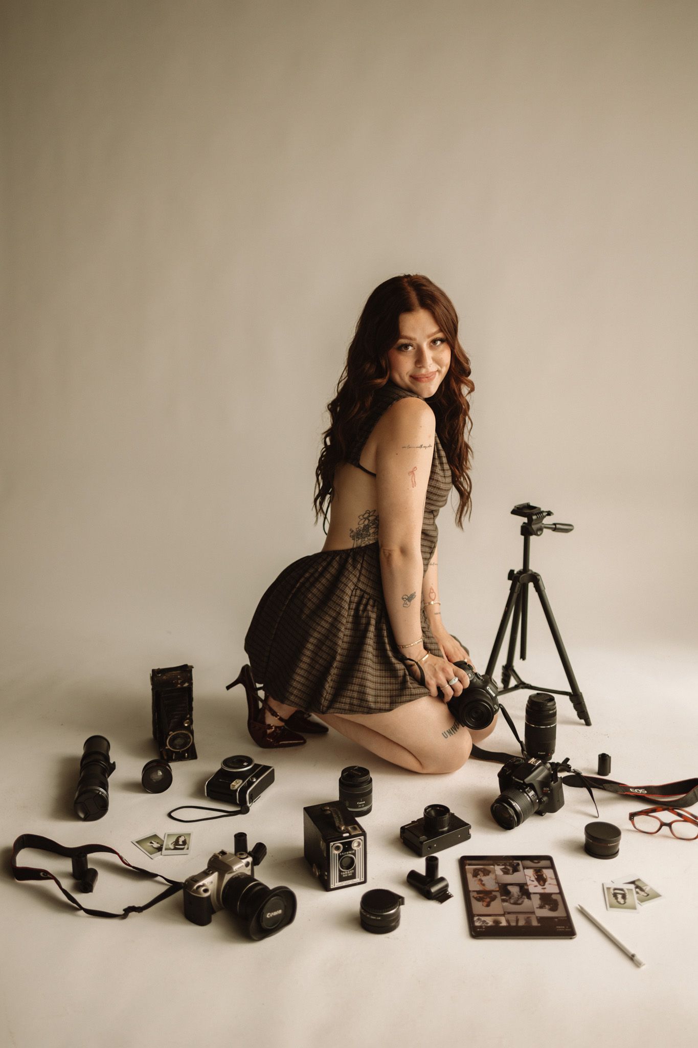 A series of sequential photographs showing a person posing with vintage cameras and photography equipment against a beige backdrop.