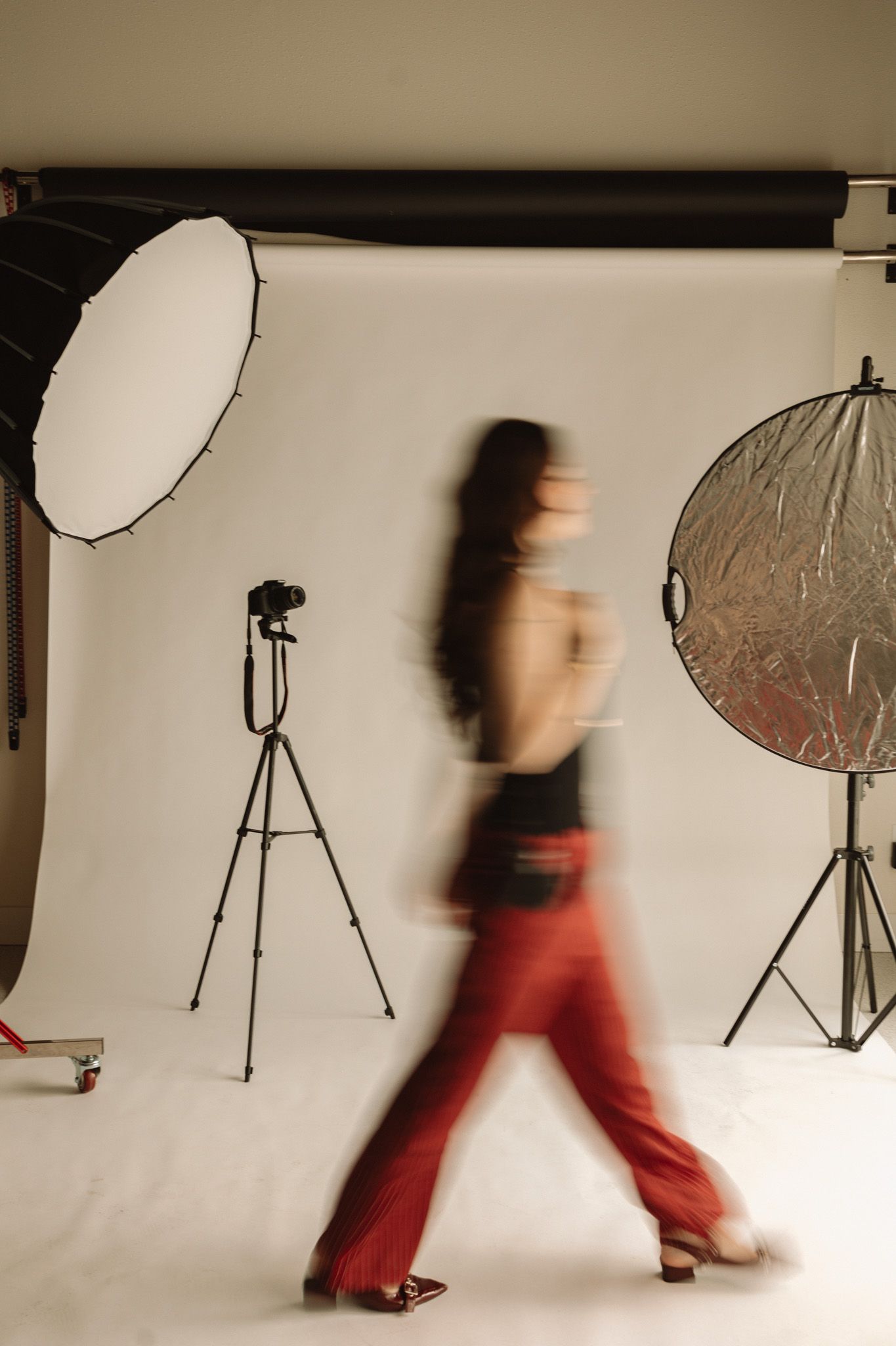 Motion-blurred figure walking past photography studio setup with reflectors and lighting equipment against white backdrop.