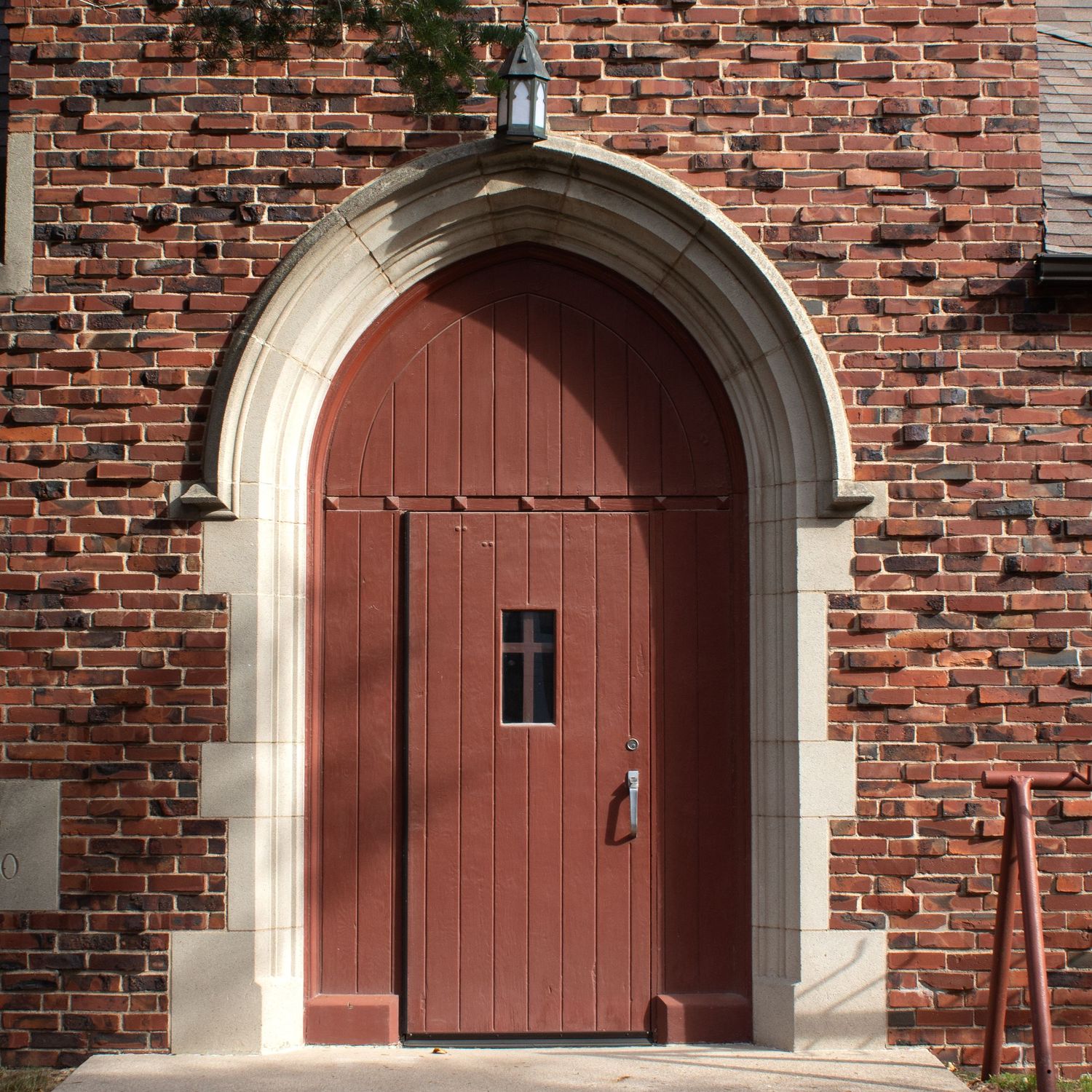 Arched wooden doorway with dark red paint and stone trim set in traditional red brick church facade.