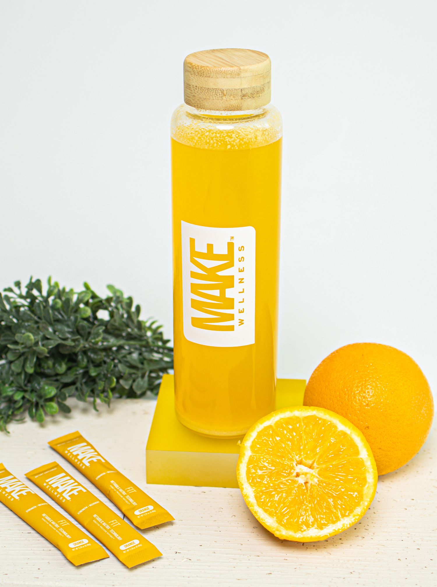 Fresh orange juice in a glass bottle with sliced citrus fruits and yellow branding elements on a light background.