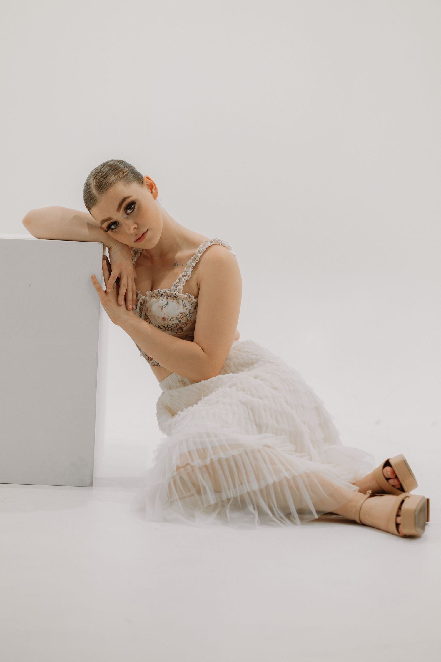 Figure in a white tulle dress and sparkly top poses elegantly against a minimalist white backdrop.