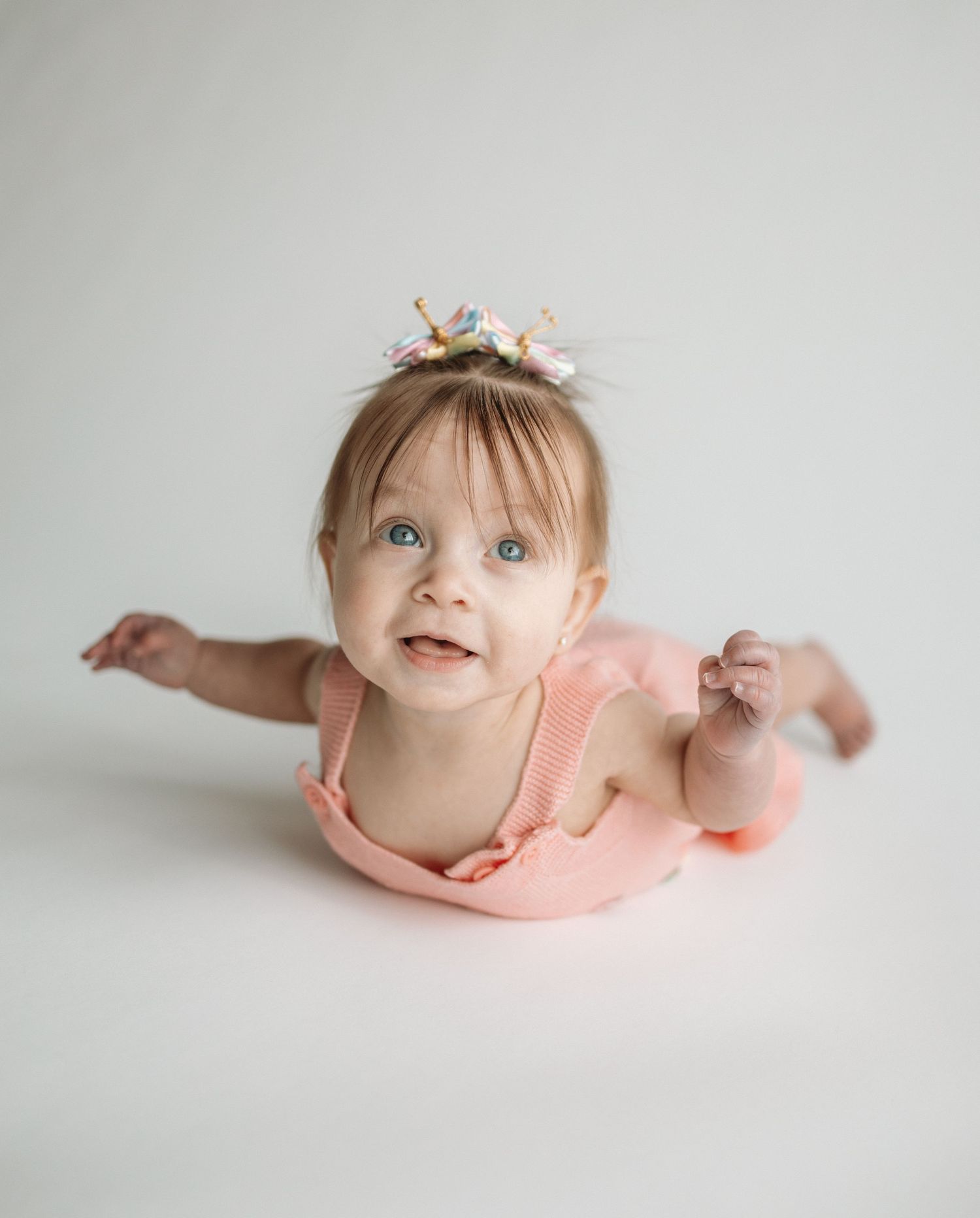 Baby in peach dress lying on white backdrop in three artistic portrait poses showing joyful expressions.
