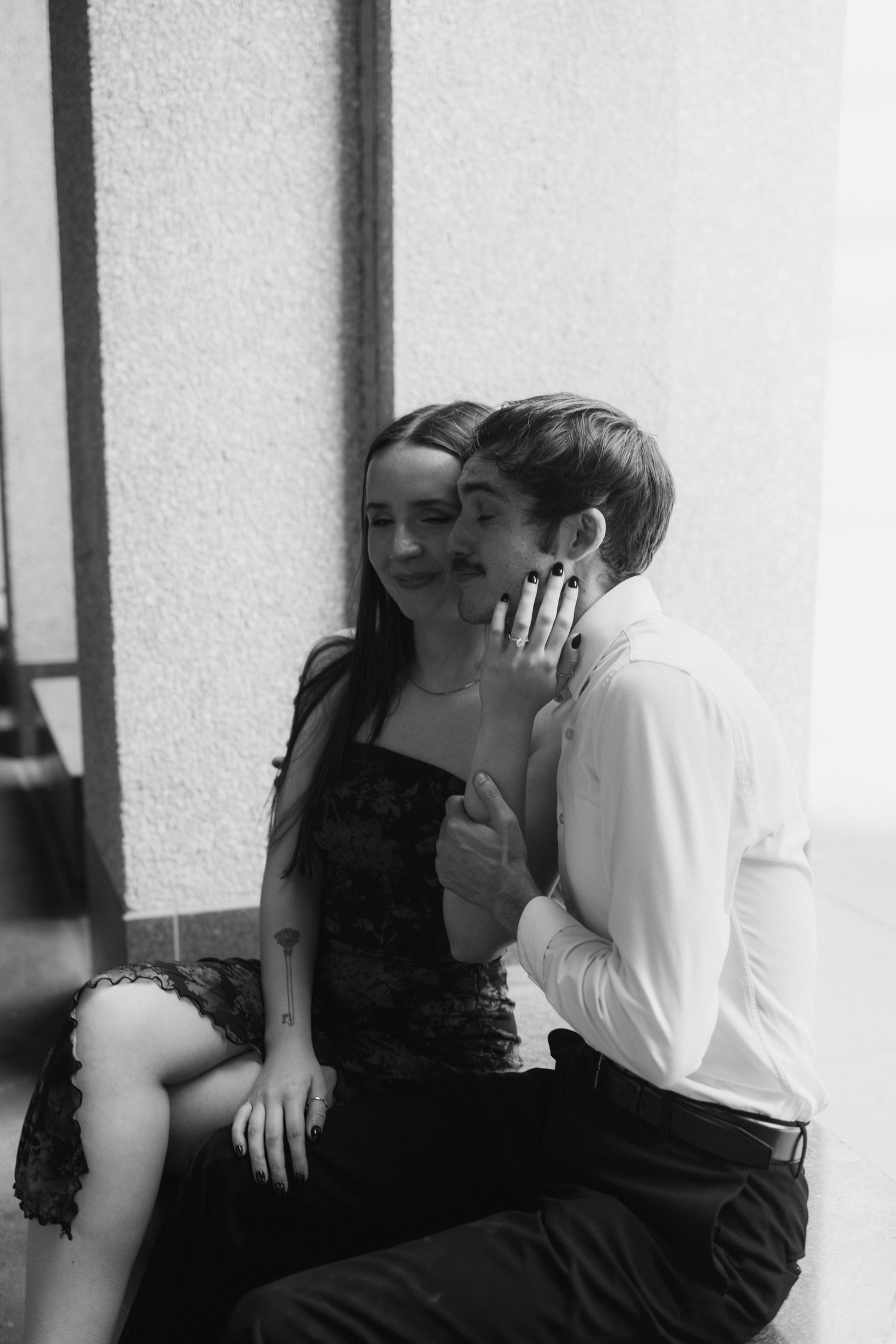 A black and white photo series showing a couple sharing intimate romantic moments against a white wall.