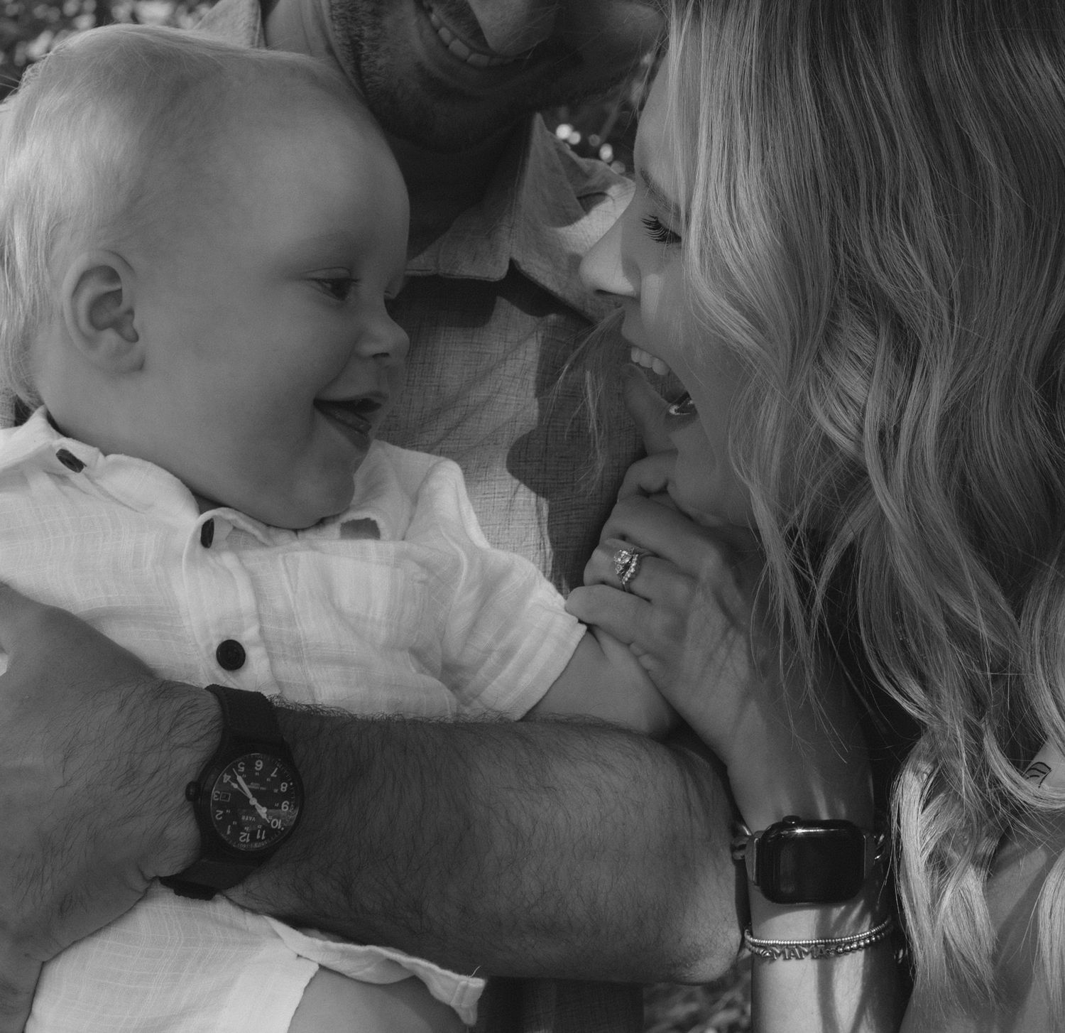 A tender black and white family moment showing a baby smiling while being held in a loving embrace.