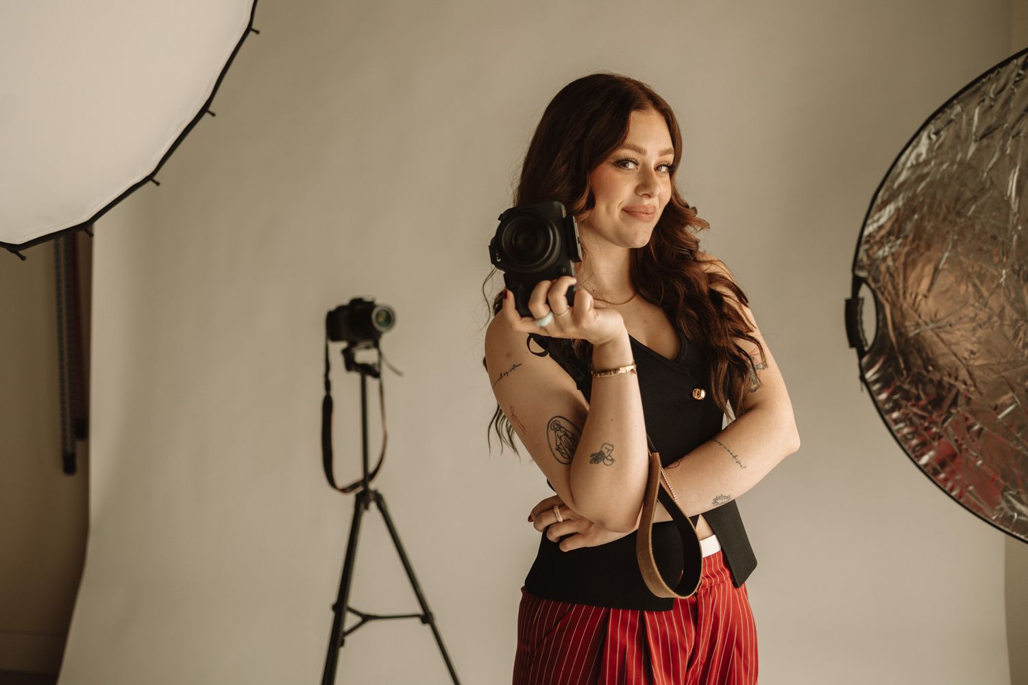 Professional photo shoot with model in red dress and photo studio lighting equipment on beige background.