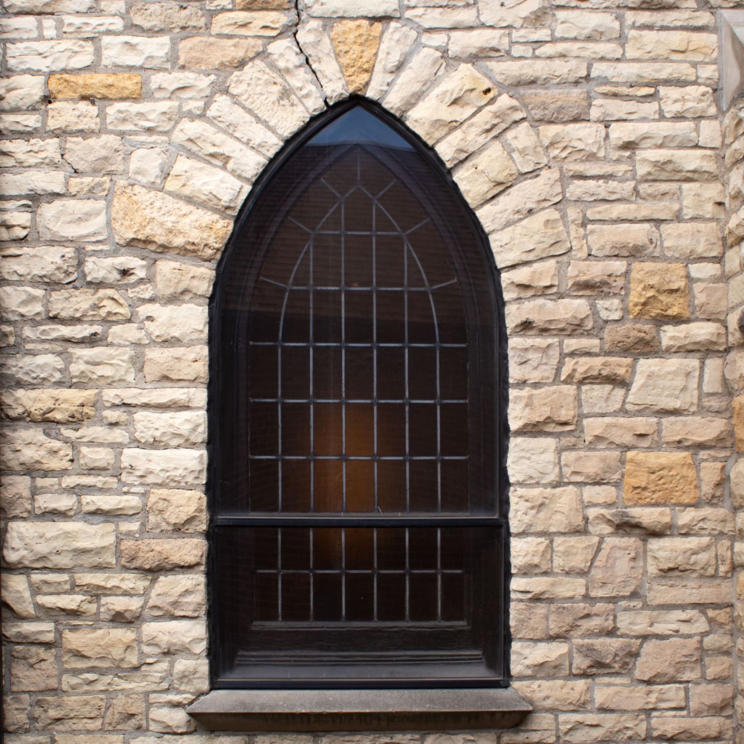 Gothic arched window with black metal grating set in a rustic limestone wall of a church or castle.