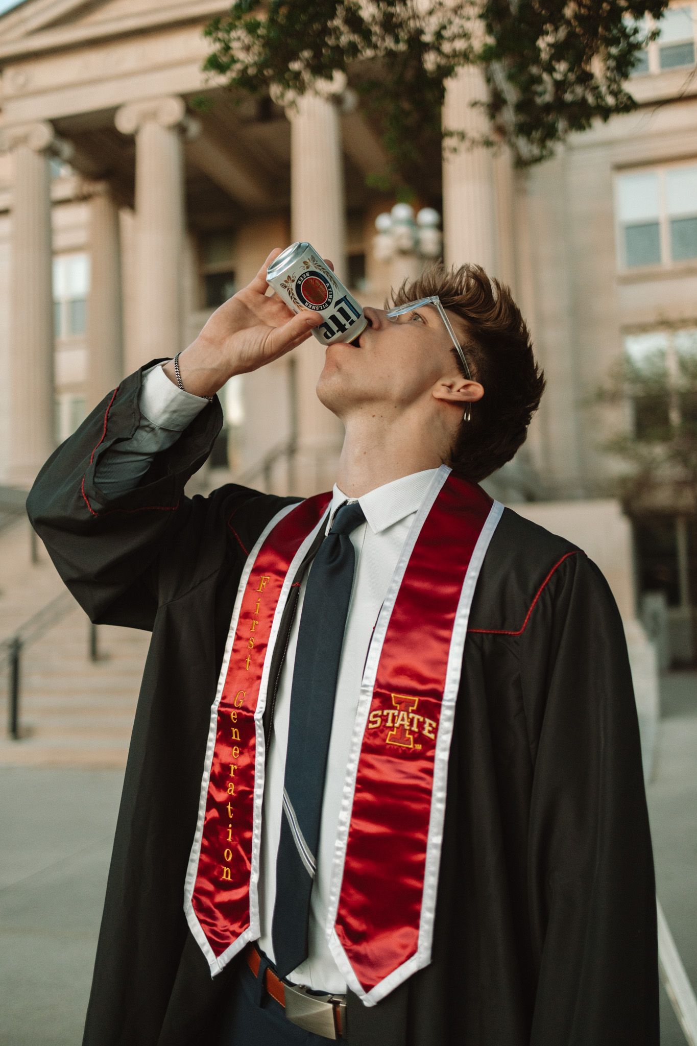 Graduate in black gown with red sash drinks from water bottle in sequence of four photos outside building.