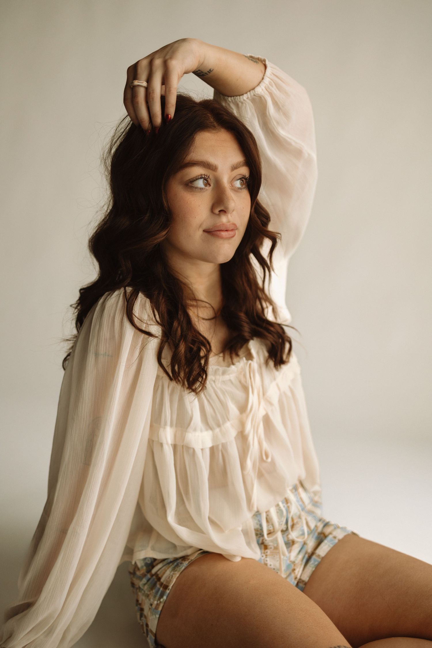 A fashion editorial series showing a model in soft lighting wearing a romantic sheer white blouse and denim shorts.