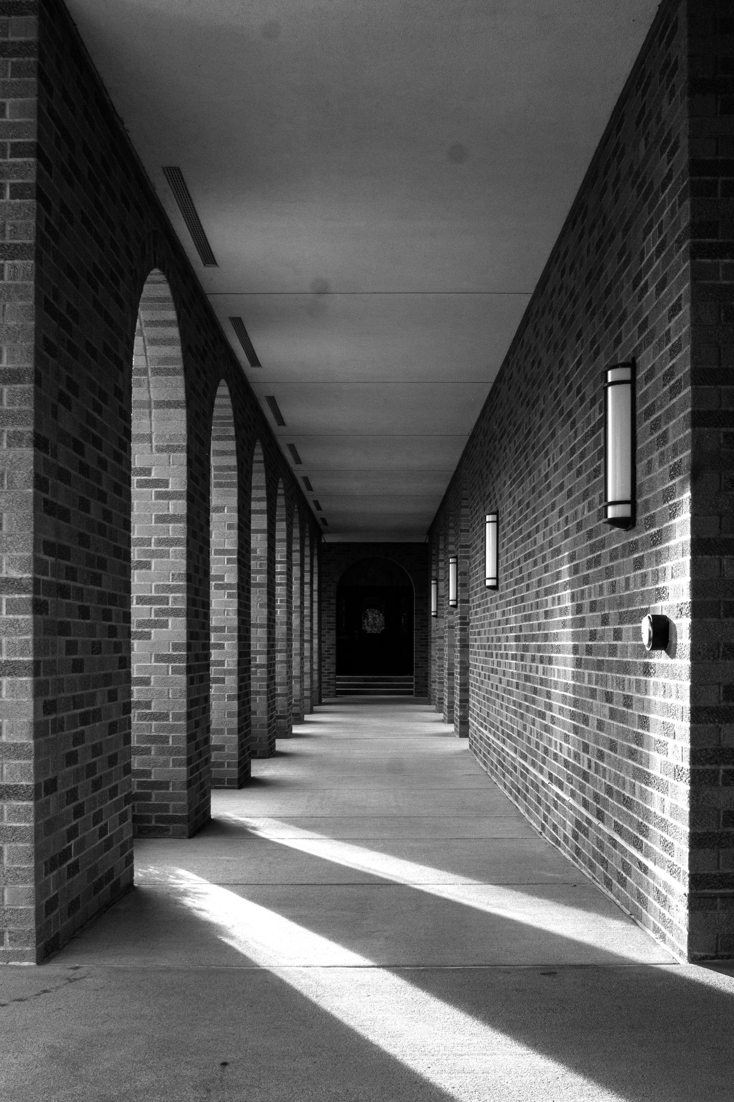 Dramatic black and white architectural hallway with brick walls and diagonal light patterns from wall-mounted sconces.