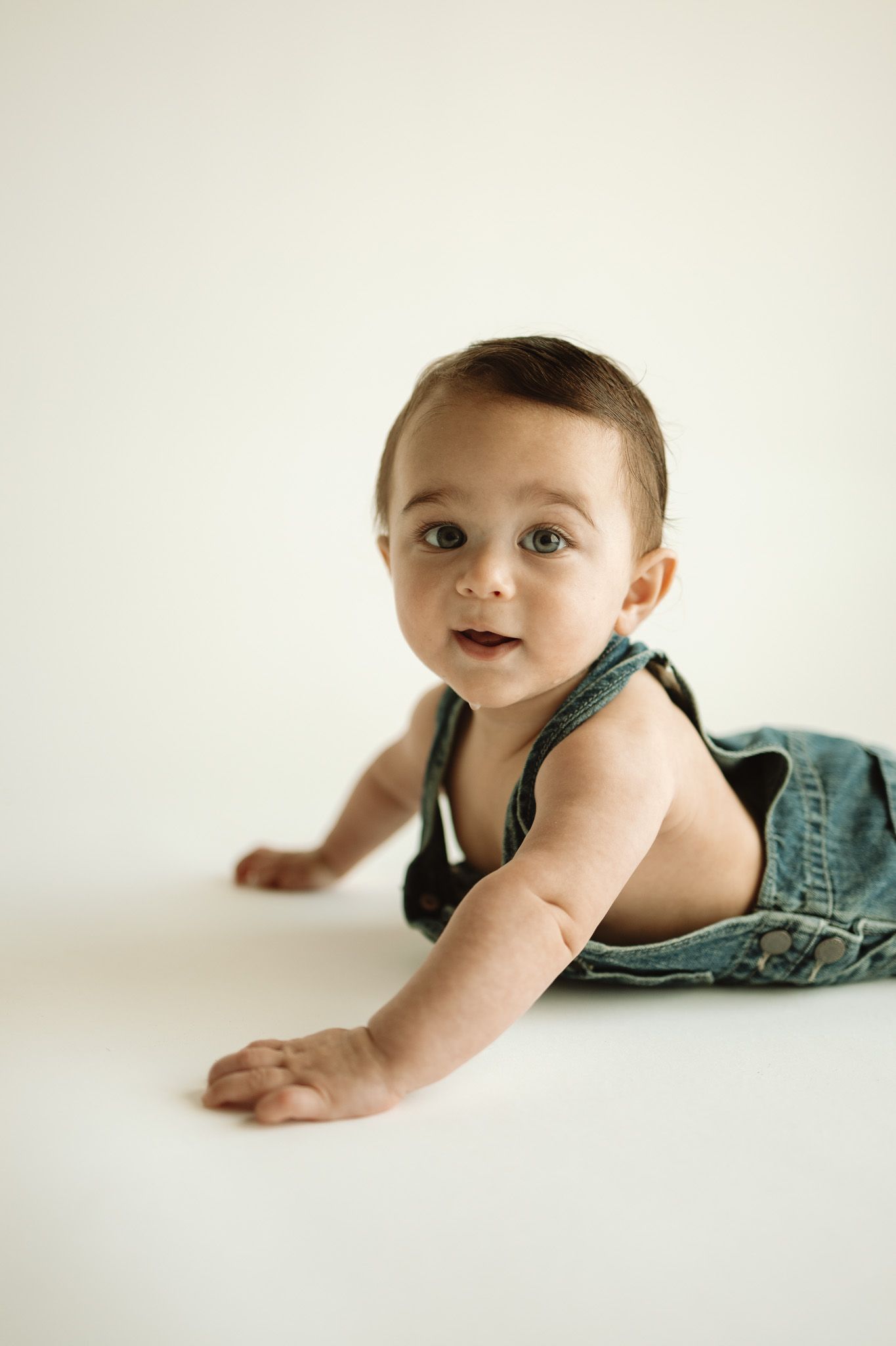 Four sequential photos show a baby in denim crawling and reaching forward on a white surface.