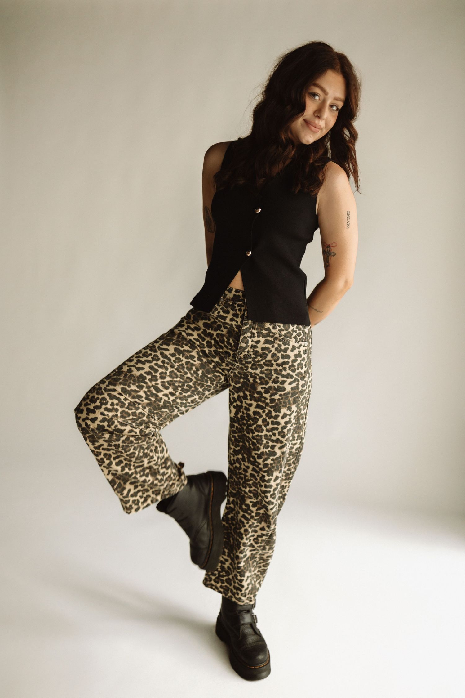 Figure strikes dynamic poses wearing black turtleneck and leopard print pants with chunky platform boots against white backdrop.