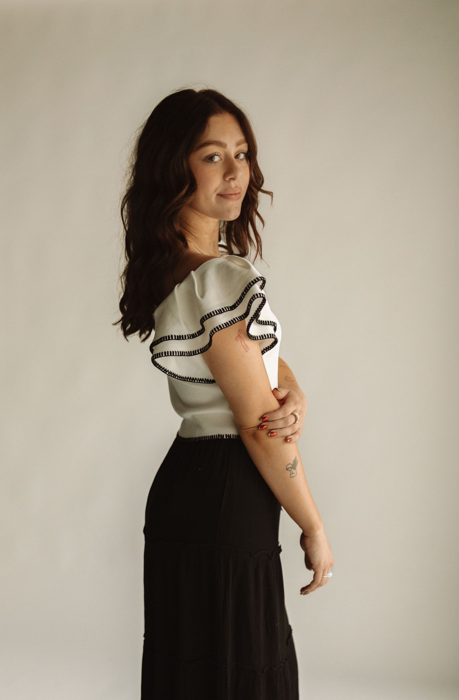 Side profile portrait of someone in a ruffled white top and flowing black skirt posed against a neutral backdrop.