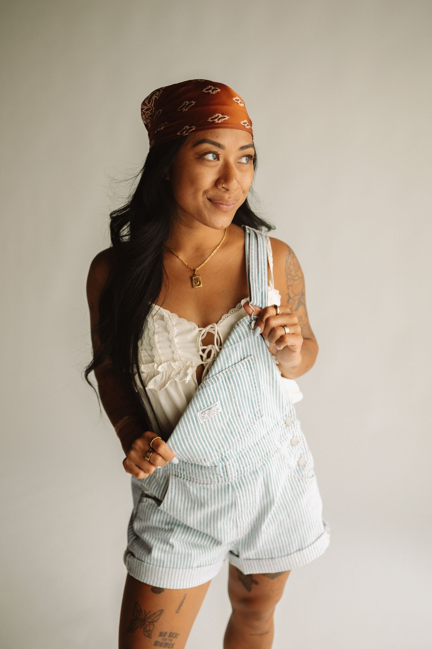 Someone wearing a red bandana, white top and striped overalls poses playfully against a light background.