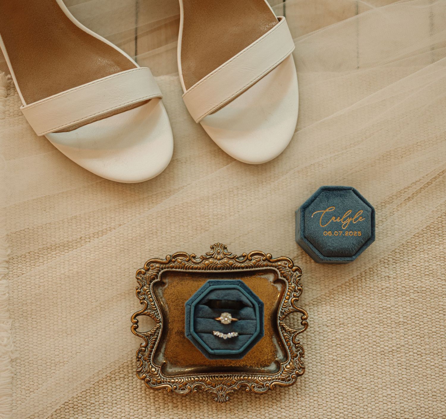 A pair of ivory bridal shoes with decorative frames and blue velvet ring boxes arranged on a neutral background.