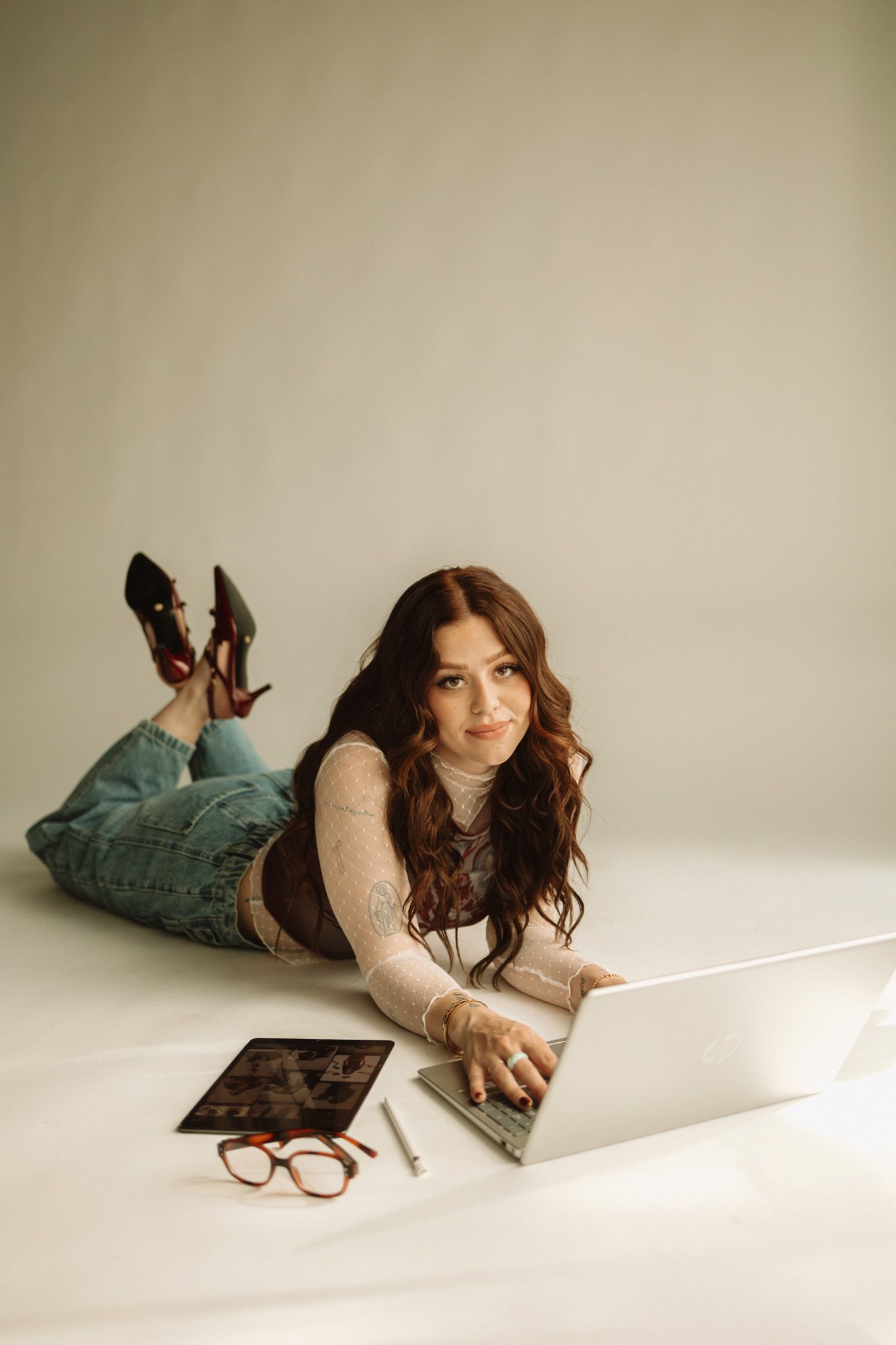 A photographer lies on the floor while working with digital equipment in a studio.