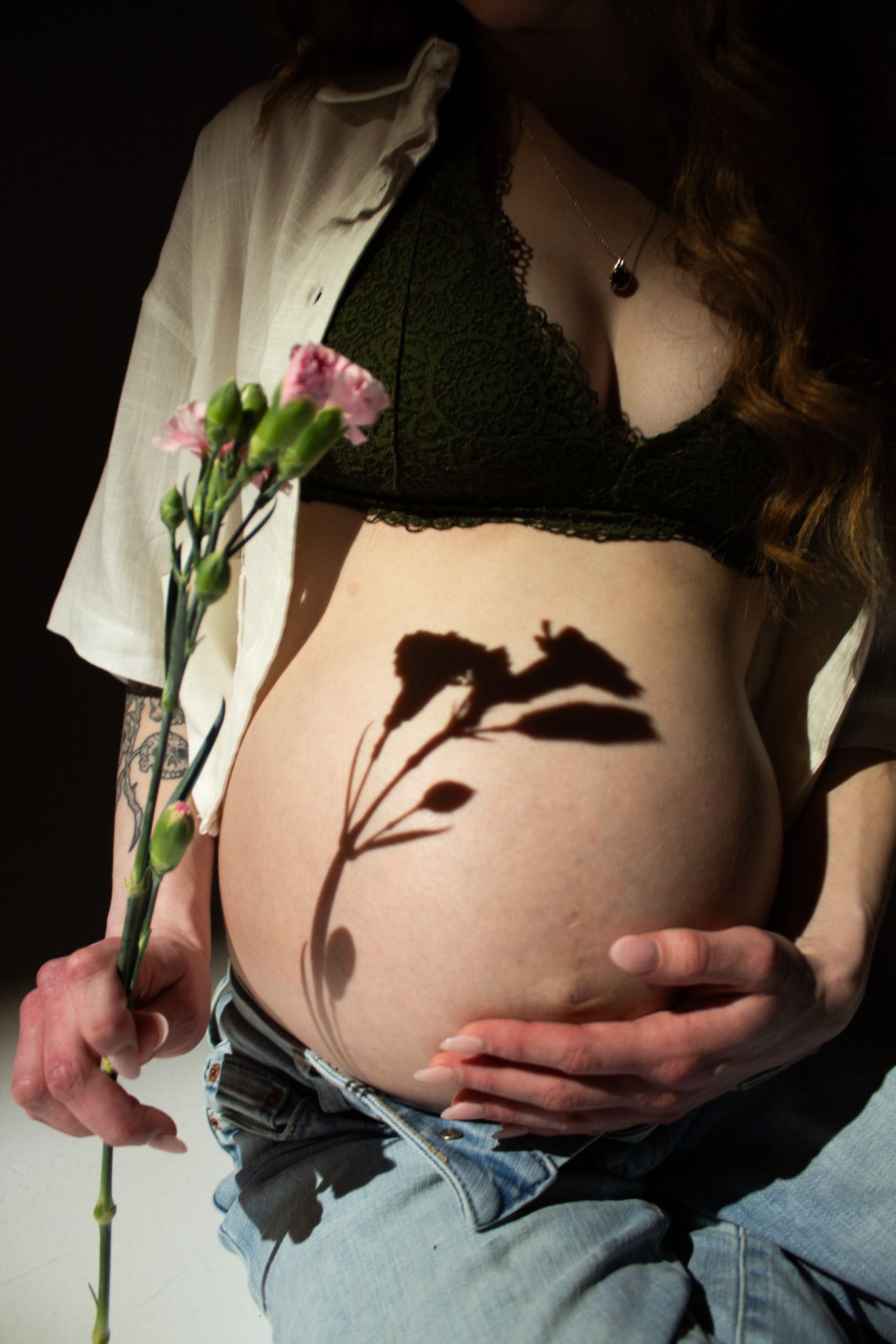 Silhouette of pink carnation flowers casting shadow on pregnant belly in artistic maternity photo.
