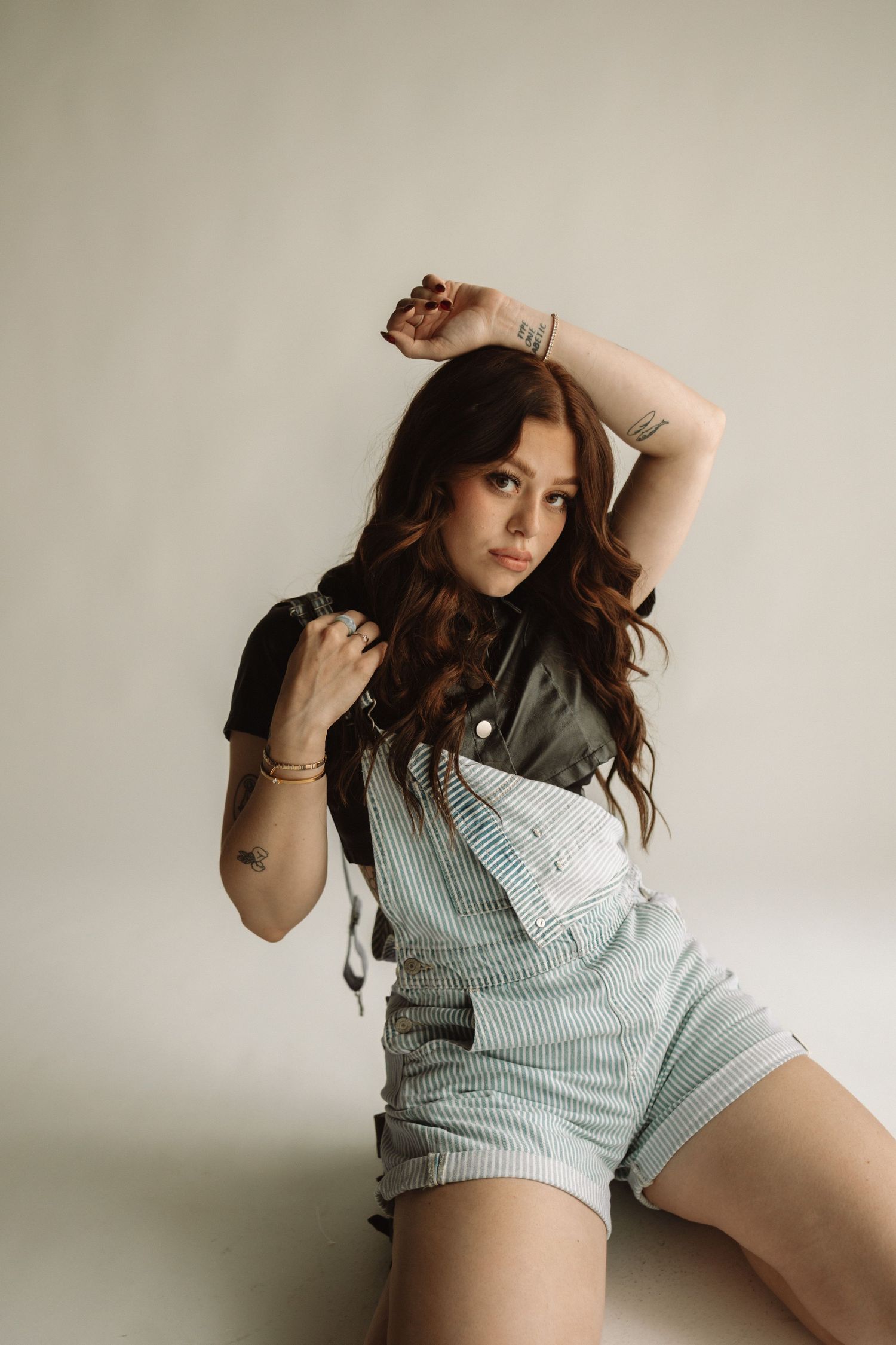 Fashion model in pale gray pinstriped button-down shirt poses against minimalist studio backdrop in photoshoot series.