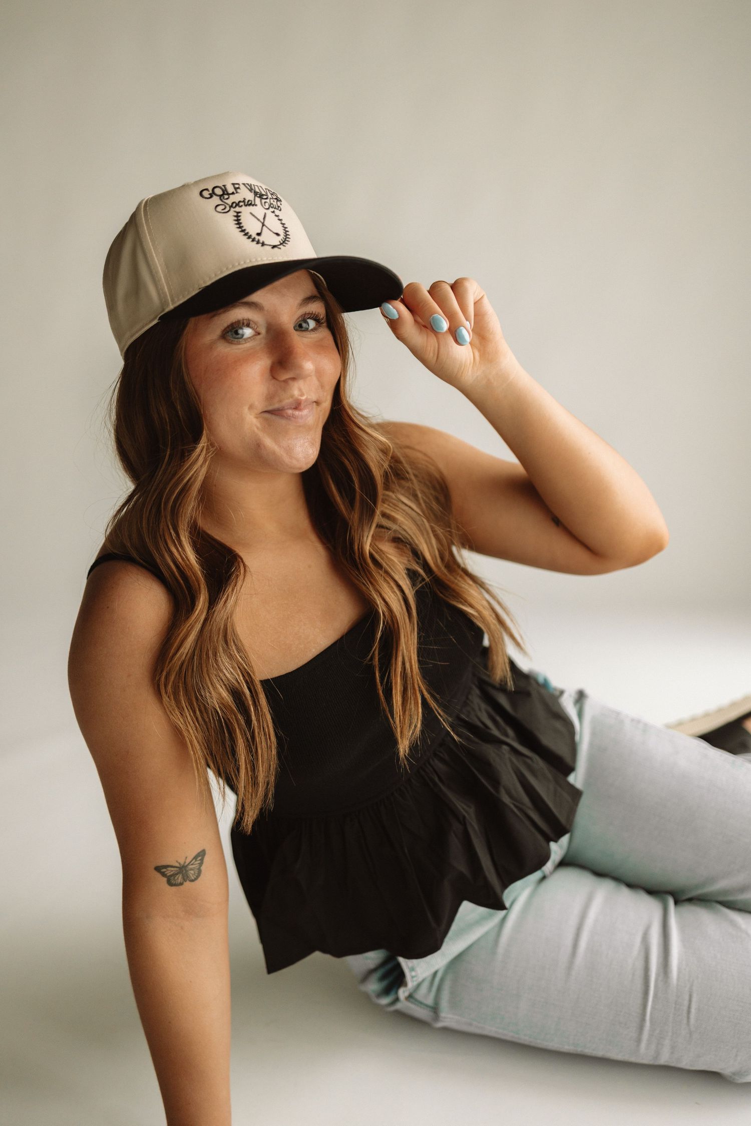 A person wearing a beige baseball cap and black tank top poses casually in a series of photos against a light background.
