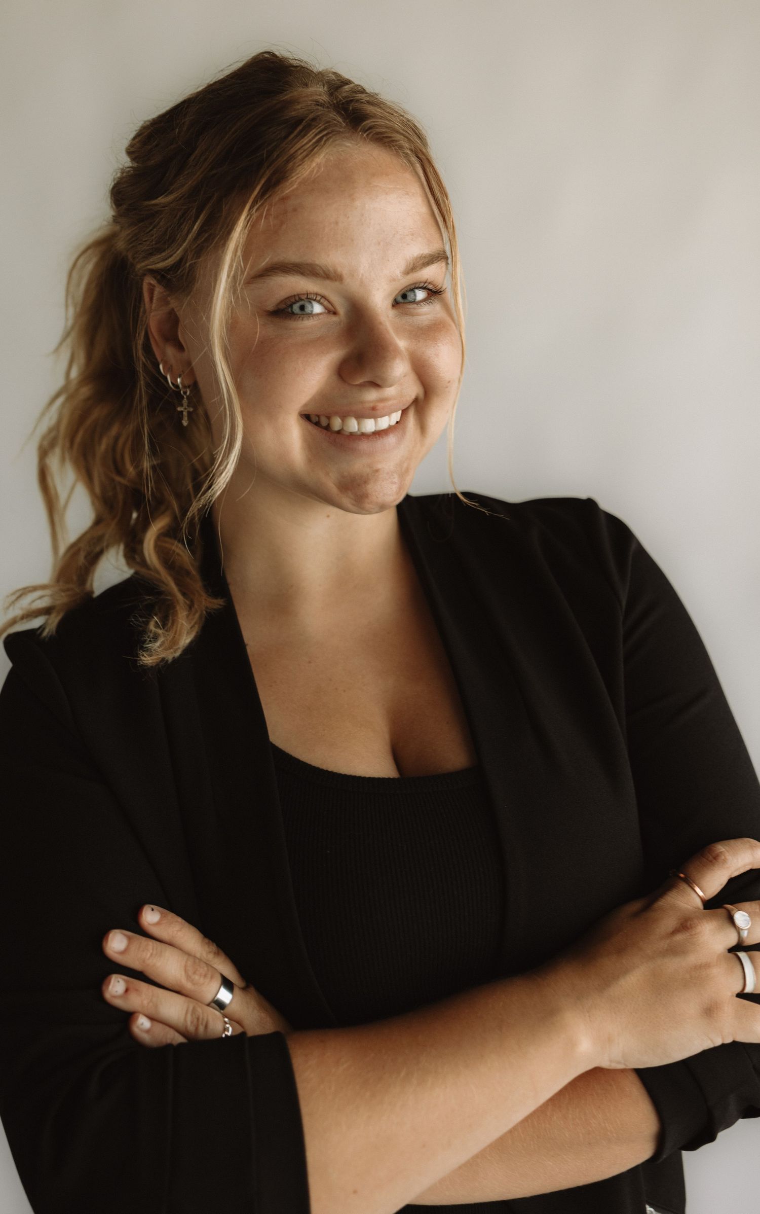 Professional portrait of a person in a black blazer and top smiling warmly against a light gray background.