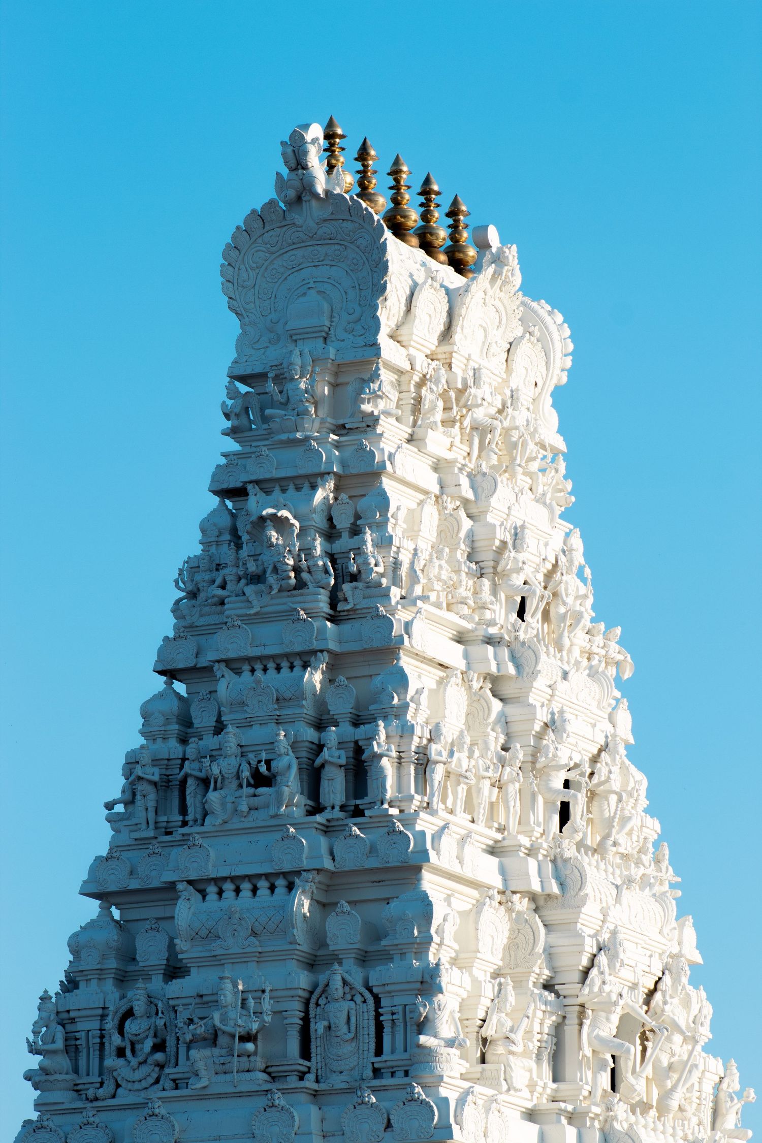 White Hindu temple gopuram tower with intricate carvings rises against bright blue sky at Venkateshwara Temple.