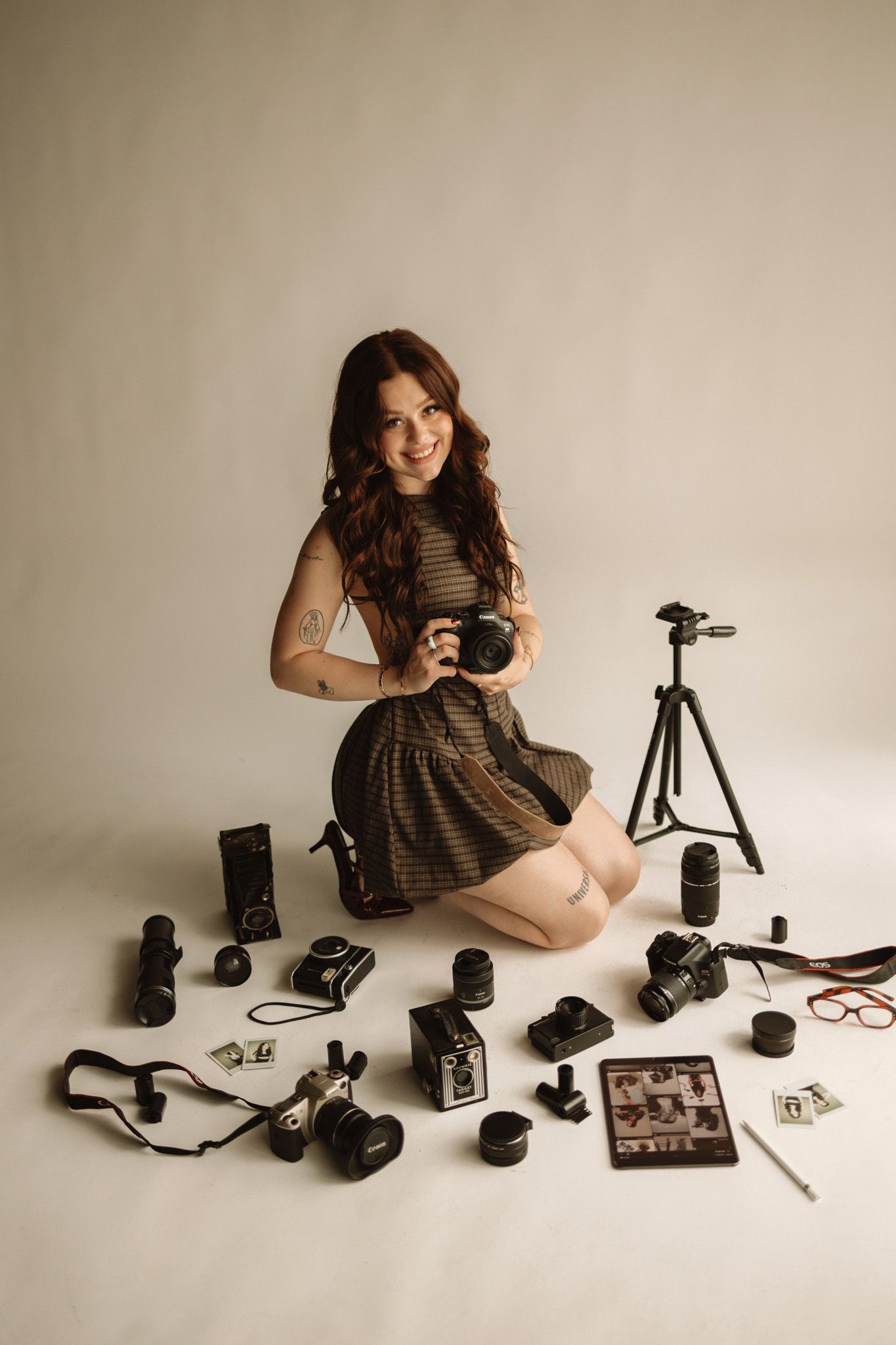 A photographer with photography equipment including cameras, lenses, tripod and accessories arranged on a light background.