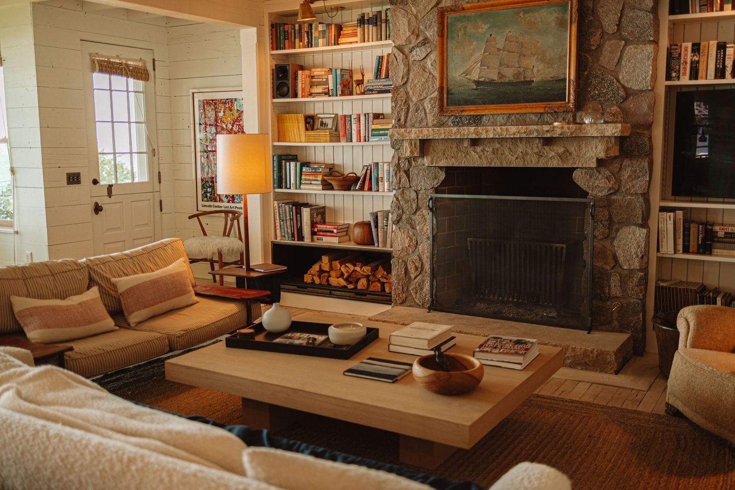 A cozy living room features stone walls, leather furniture, and built-in wooden shelving with warm ambient lighting.