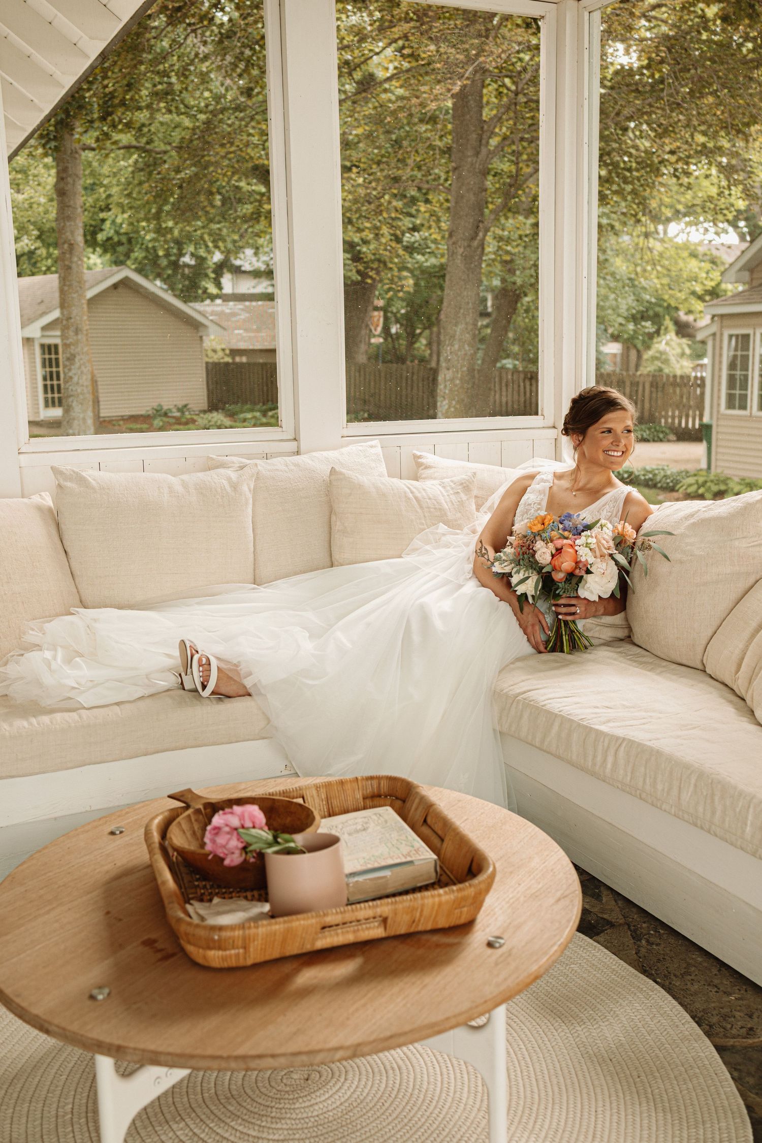 White cushioned porch seating area arranged with wooden serving trays in a sunlit outdoor space.