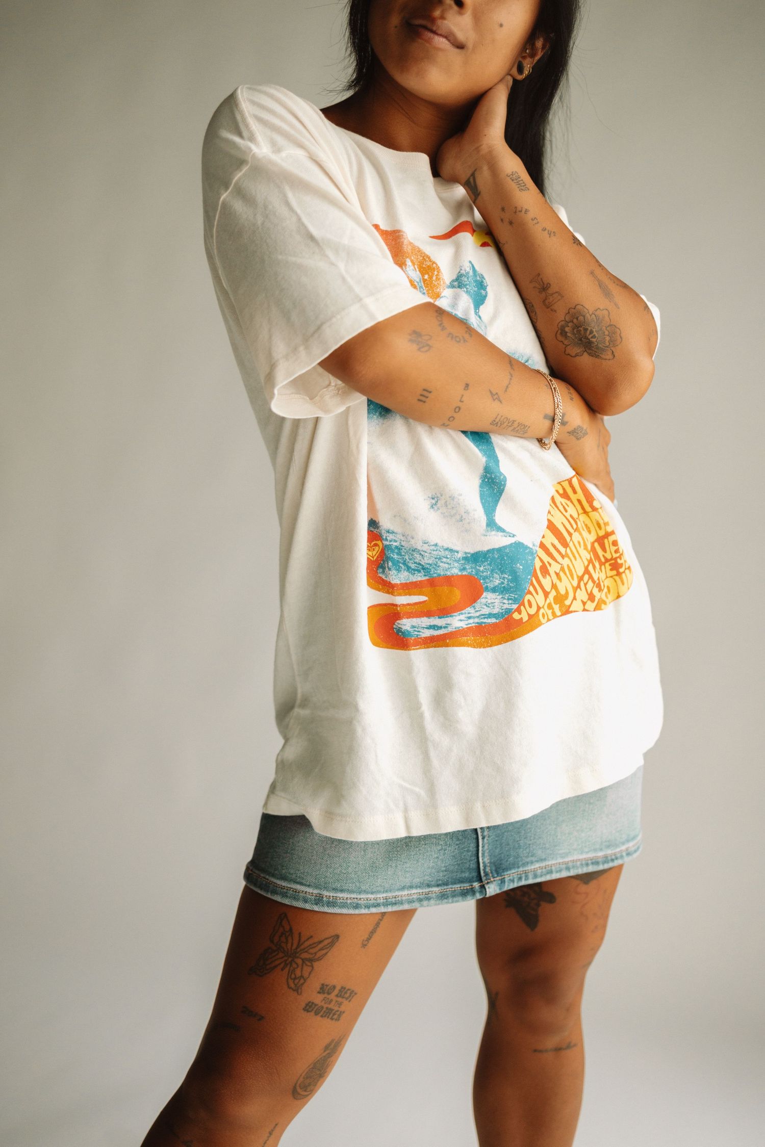 Close-up shots of a white t-shirt with retro-style orange and blue artwork worn with jean shorts.