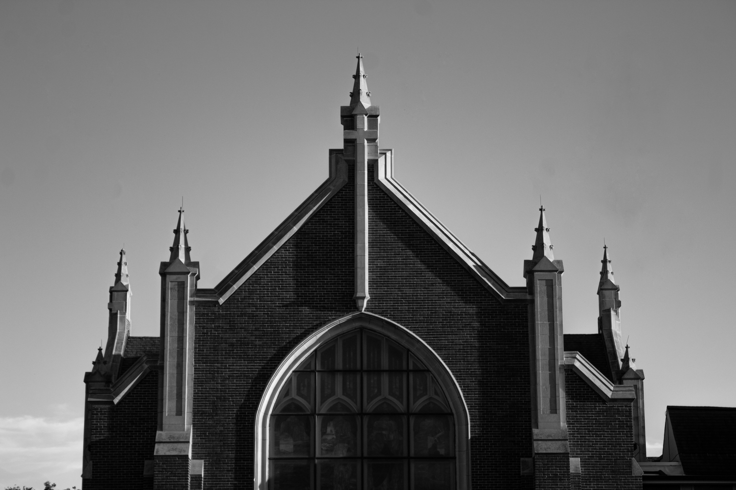 Black and white photograph of a Gothic church facade with pointed arch window and decorative spires against a cloudy sky.