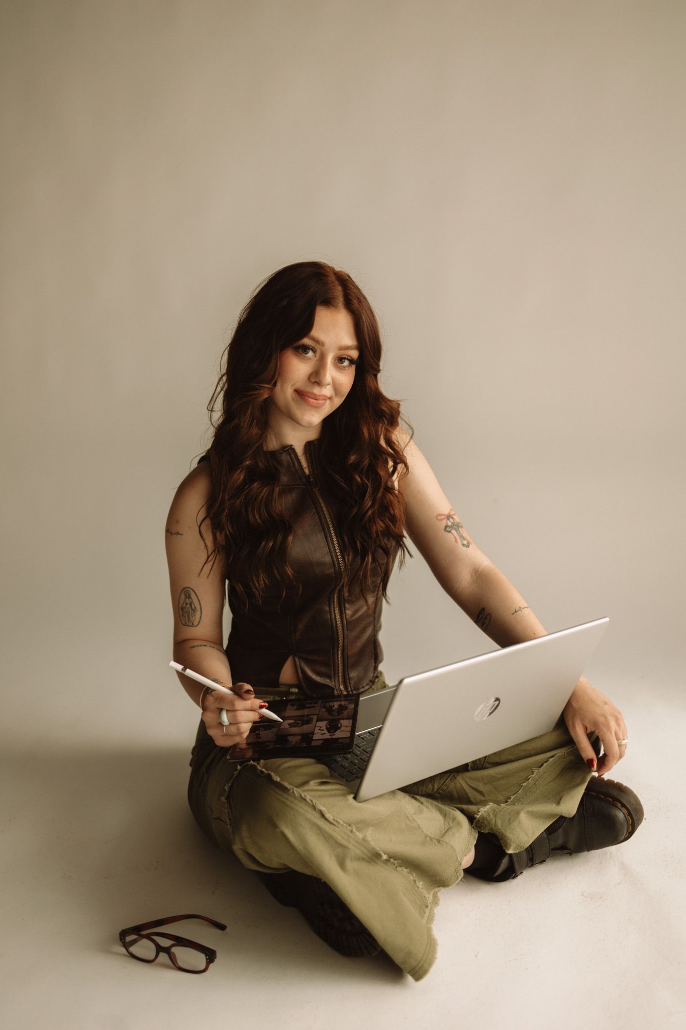 Creative professional working on laptop while sitting cross-legged in minimalist studio setting.