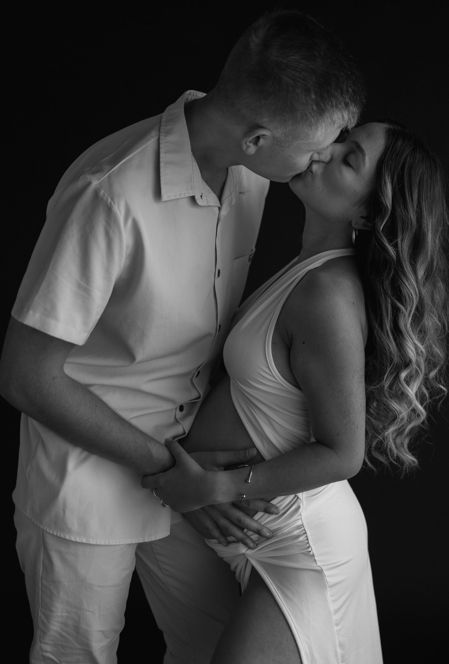 A romantic black and white portrait of two people in all white outfits sharing an intimate moment together.