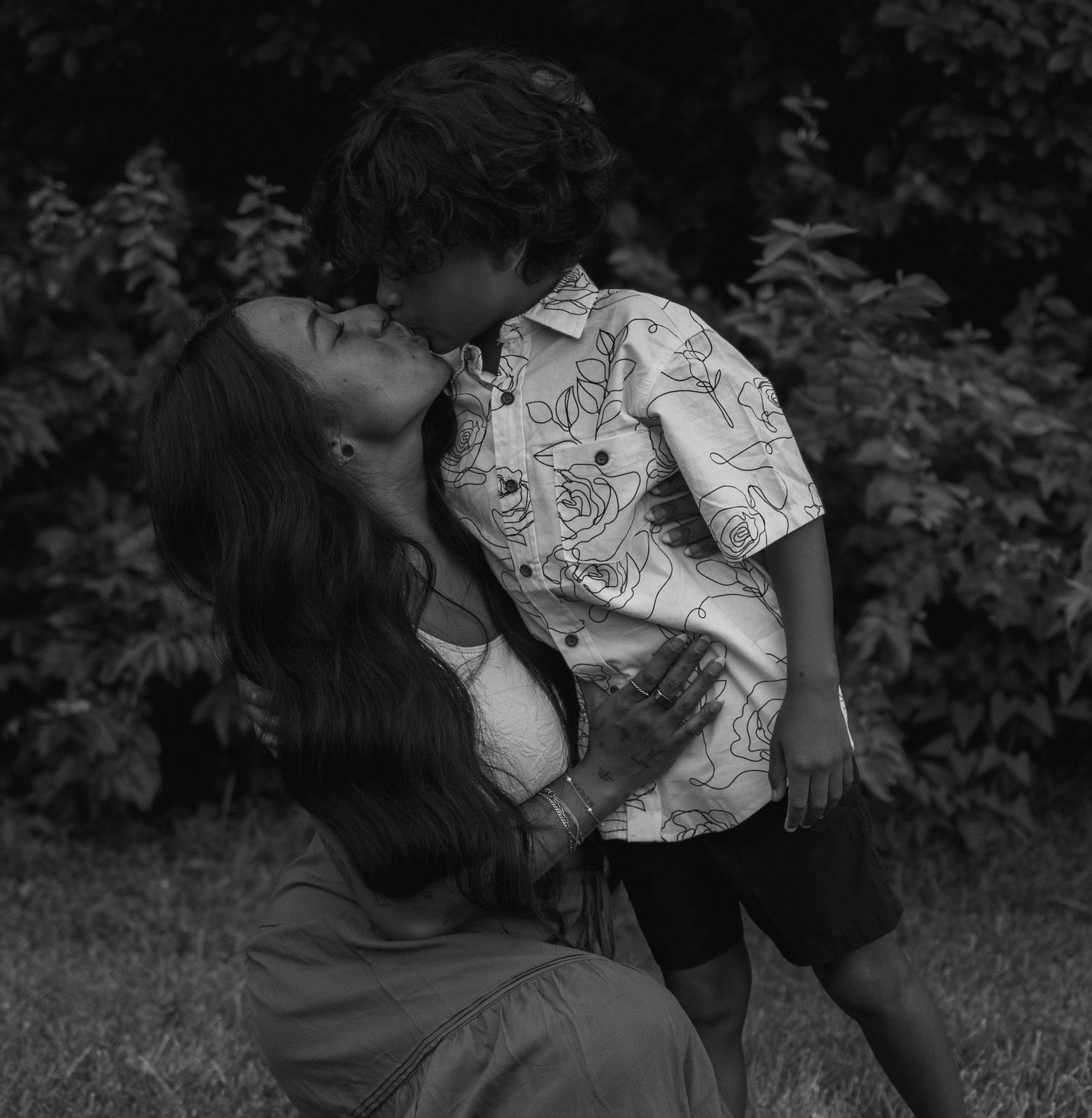 An intimate black and white portrait shows a tender moment between parent and child outdoors.