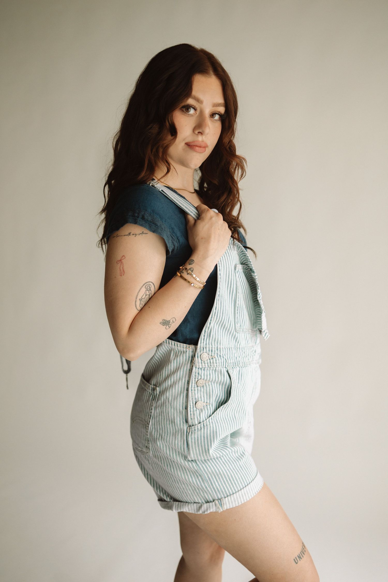 Artistic boudoir photo series showing person in denim and striped fabric posing against neutral wall.