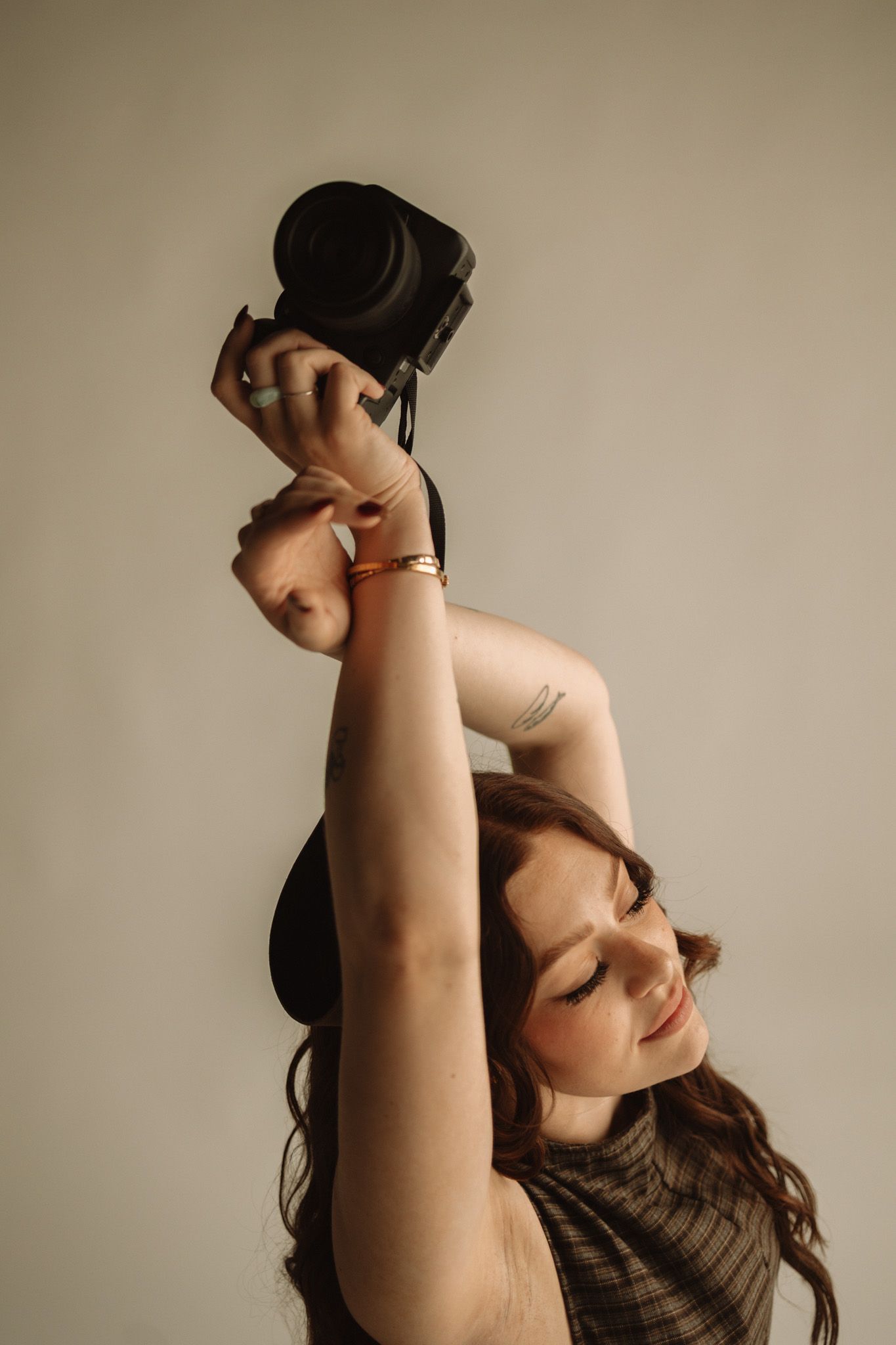 A portrait of someone in casual attire stretching their arms above their head with eyes closed in a serene pose.