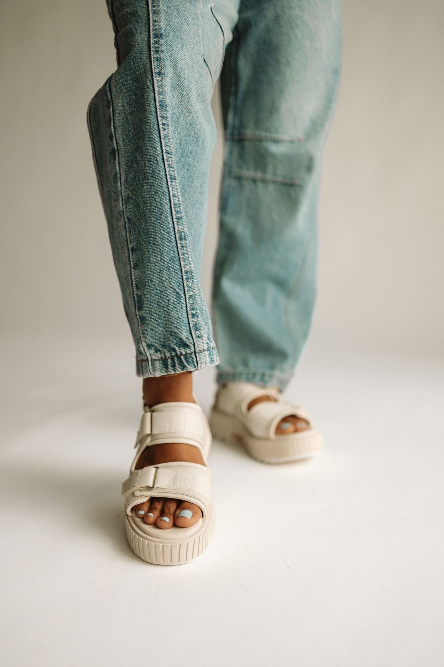 Person wearing light colored platform sandals and loose fitting light wash jeans against a neutral background.