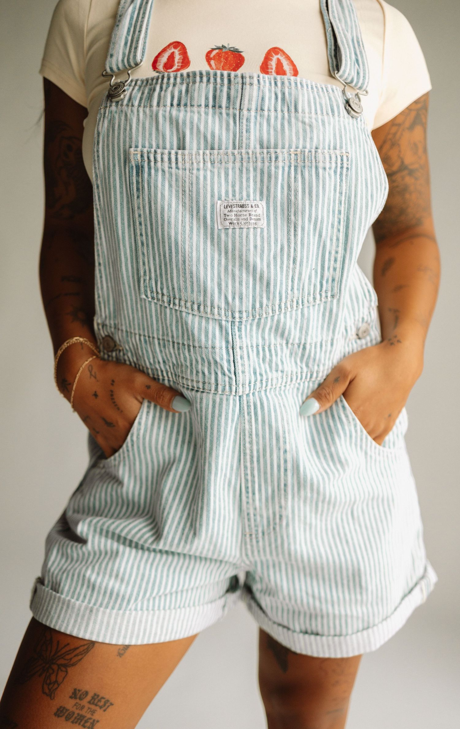 Light blue and white striped denim overalls shorts with front pocket detail and rolled cuffs.