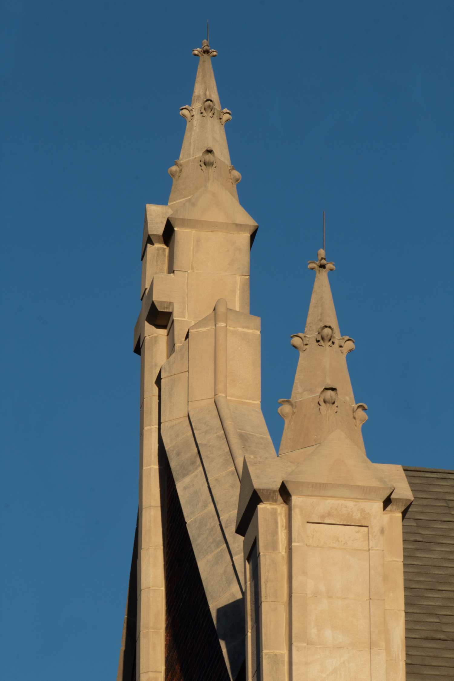 Architectural detail of two pointed church spires with Gothic-style buttresses against a deep blue sky.