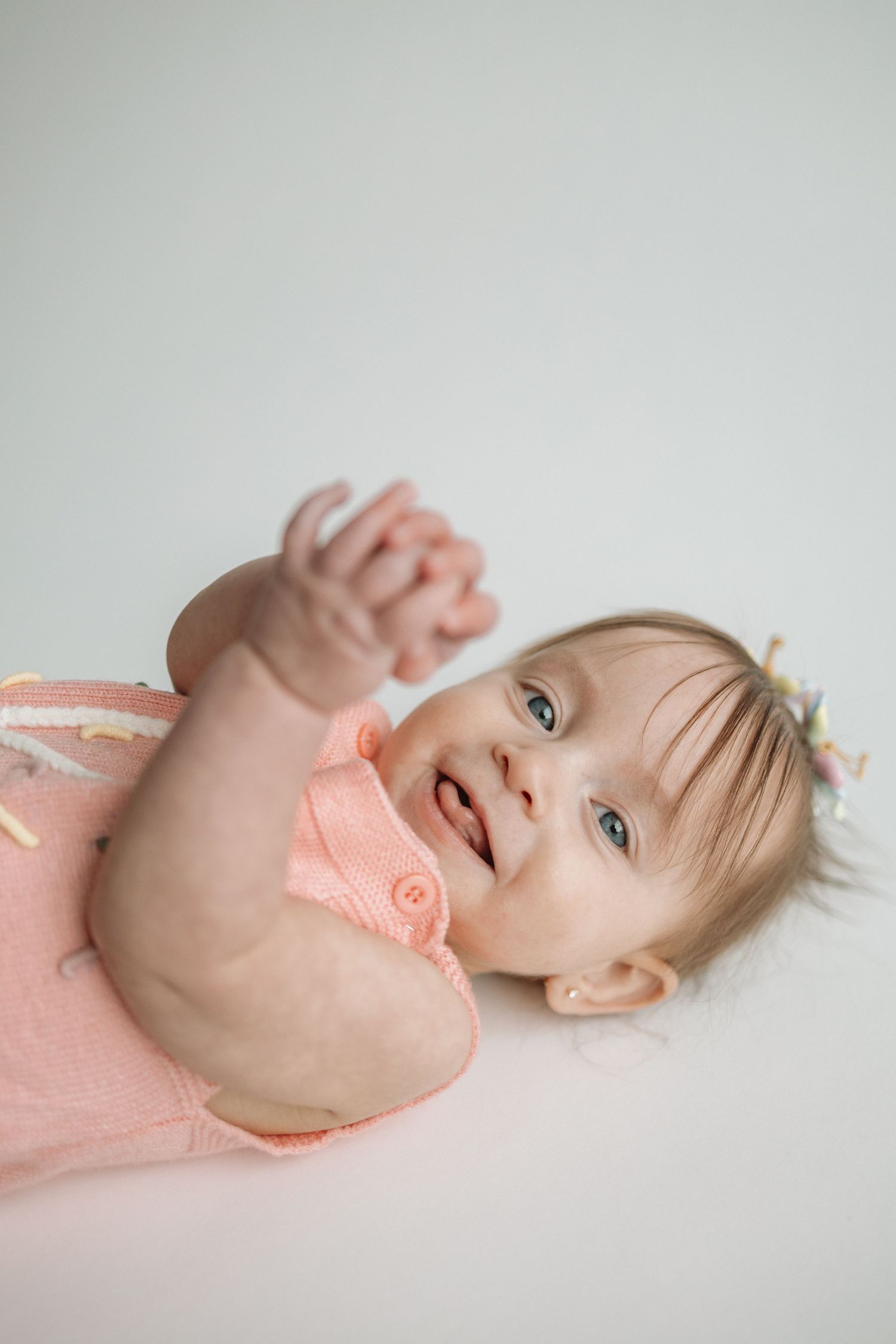 A baby in a peach-colored outfit lies on a white background in a series of playful poses.