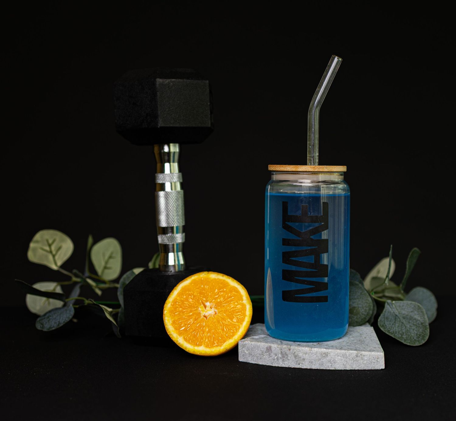 A sequence of four images showing a blue liquid in a glass beaker with an orange slice and eucalyptus leaves on a dark background.